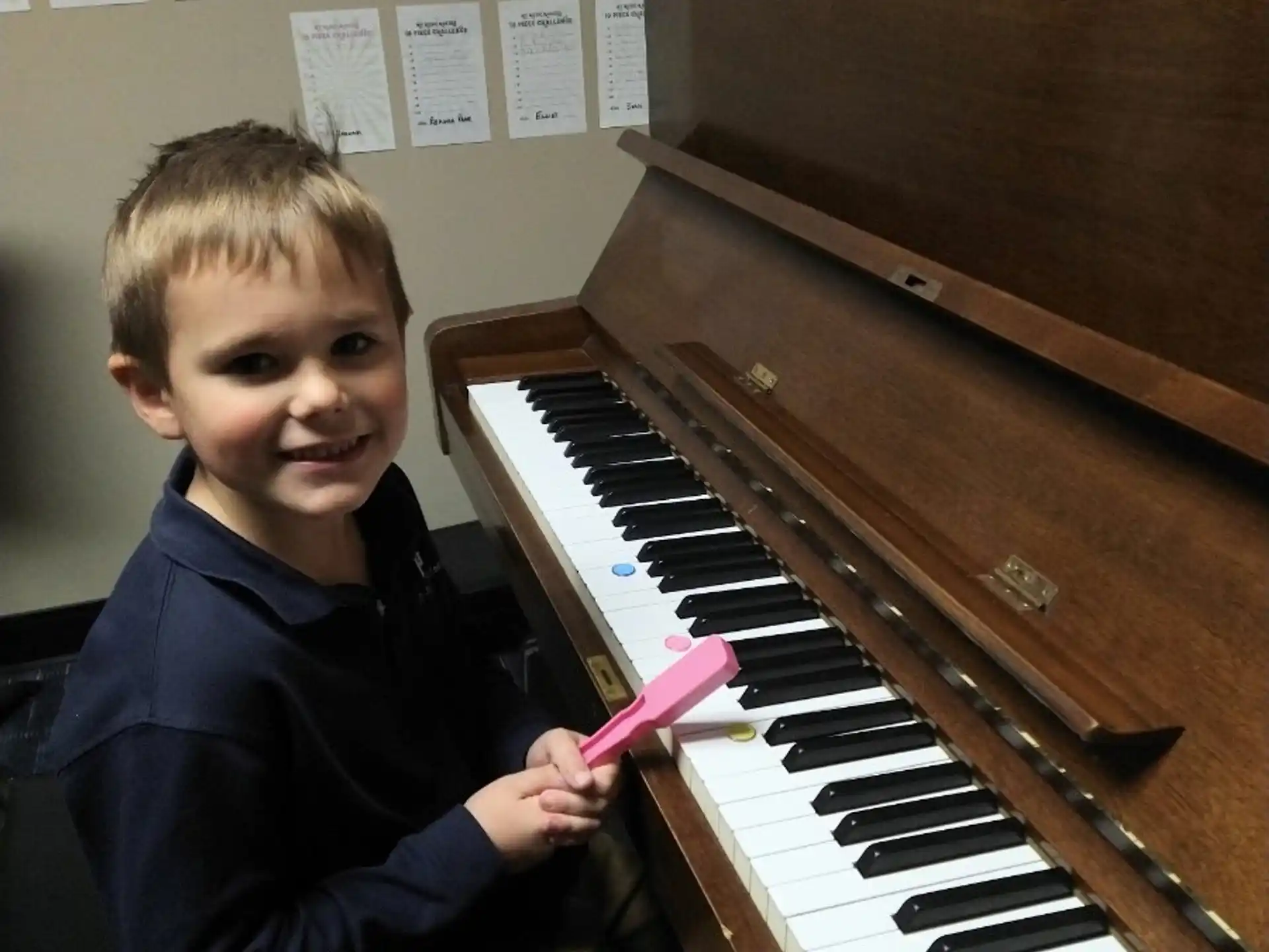 a boy holding a pink object next to a piano