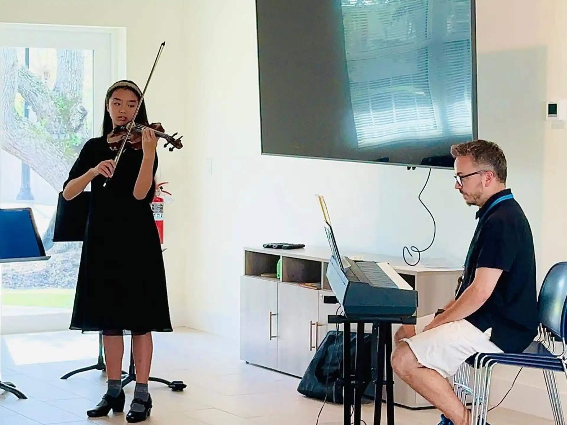a man and a woman playing a violin in a room with a projector screen and chairs