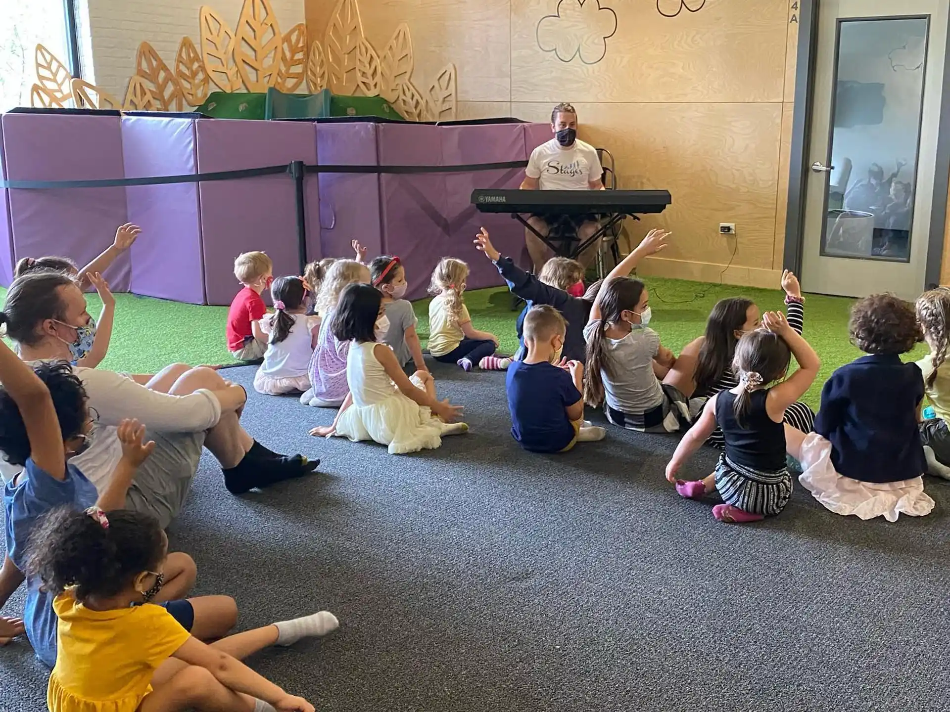 a group of children sitting on the floor in front of a person playing a guitar