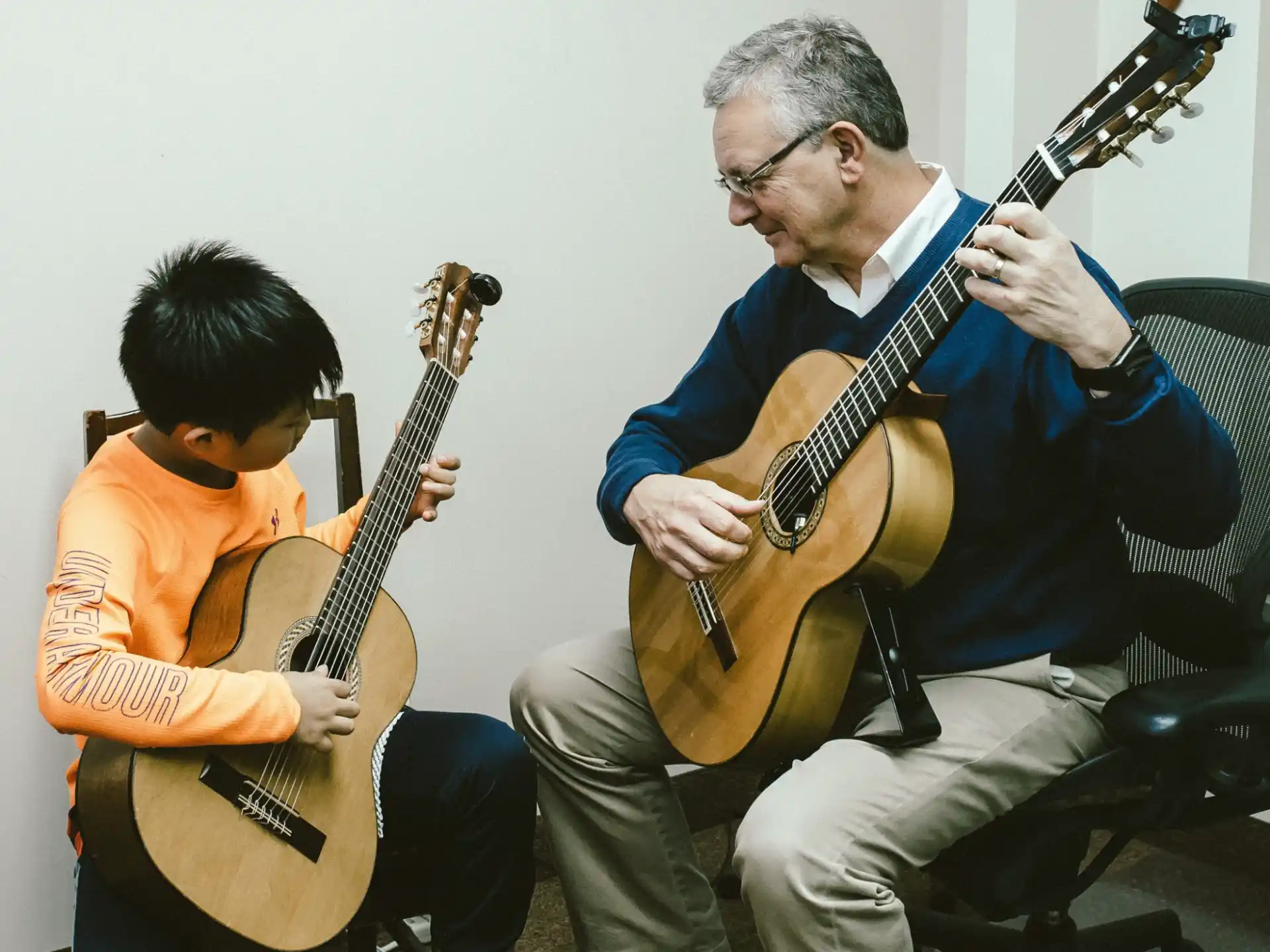 a man playing a guitar next to a boy sitting on a chair