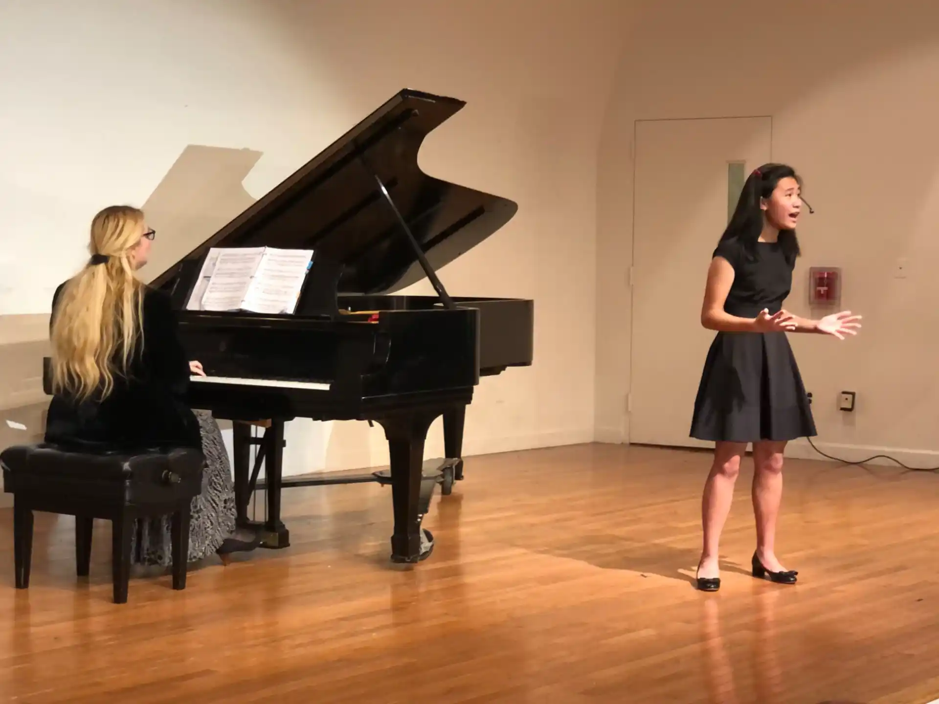 a woman standing next to a woman playing a piano