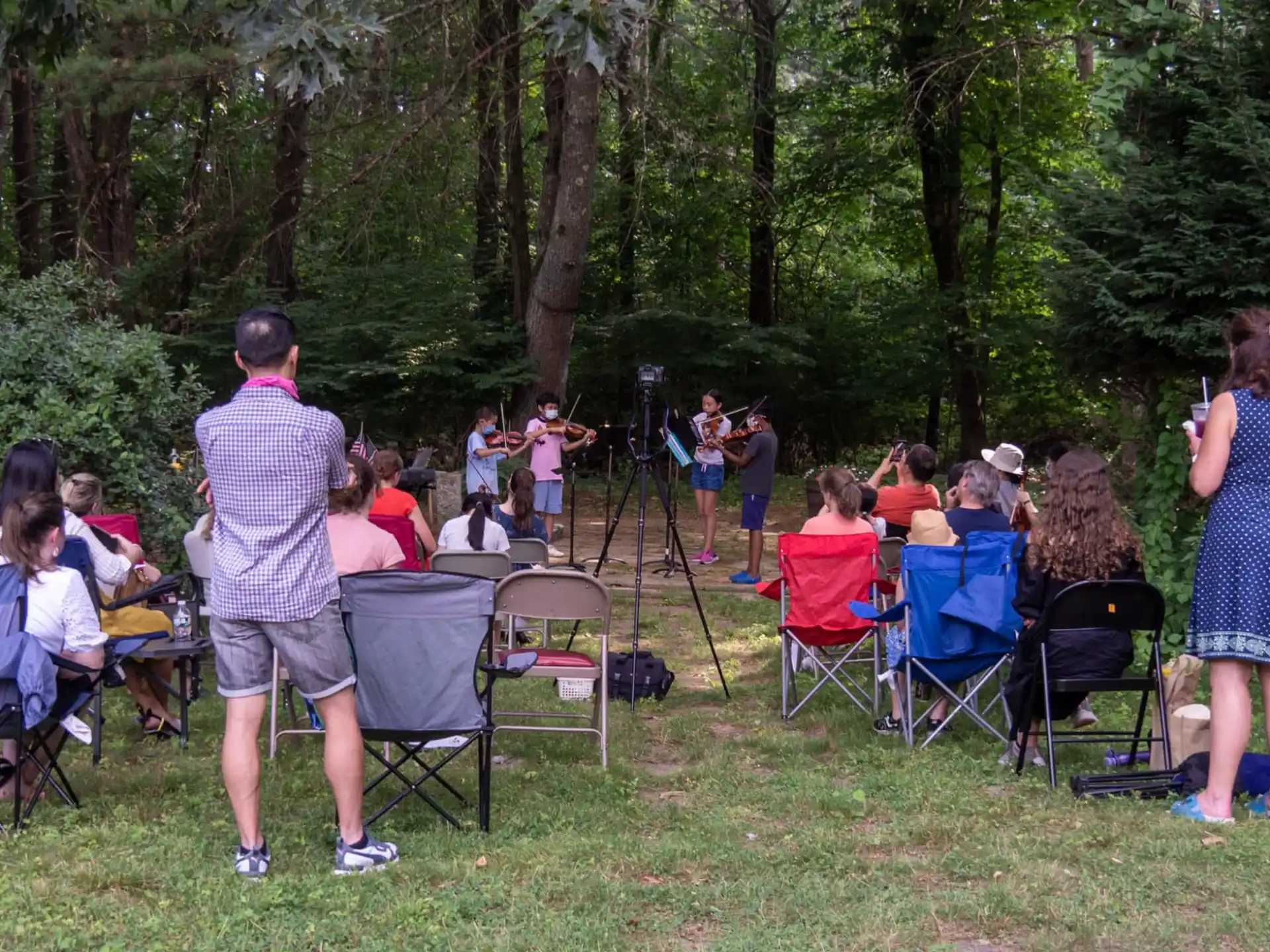 a group of people sitting in chairs in a grassy area with trees