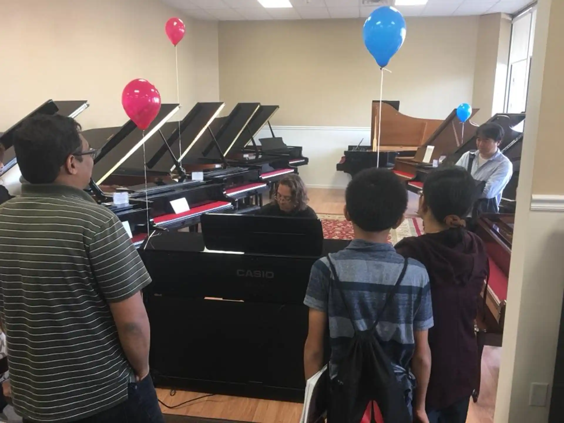 a group of people in a room with balloons and a person playing a piano