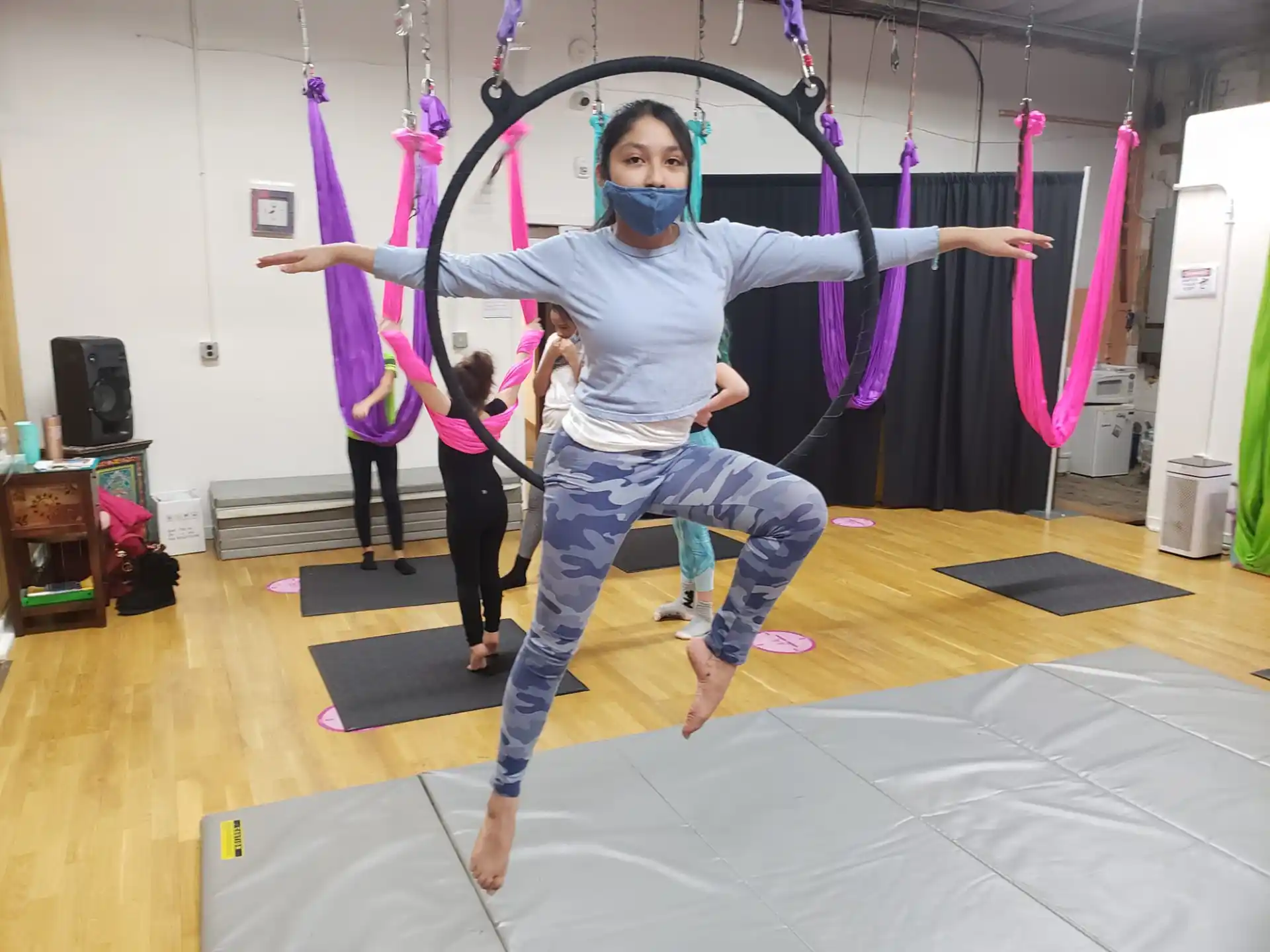 a person wearing a mask and holding the arms up in a room with other women