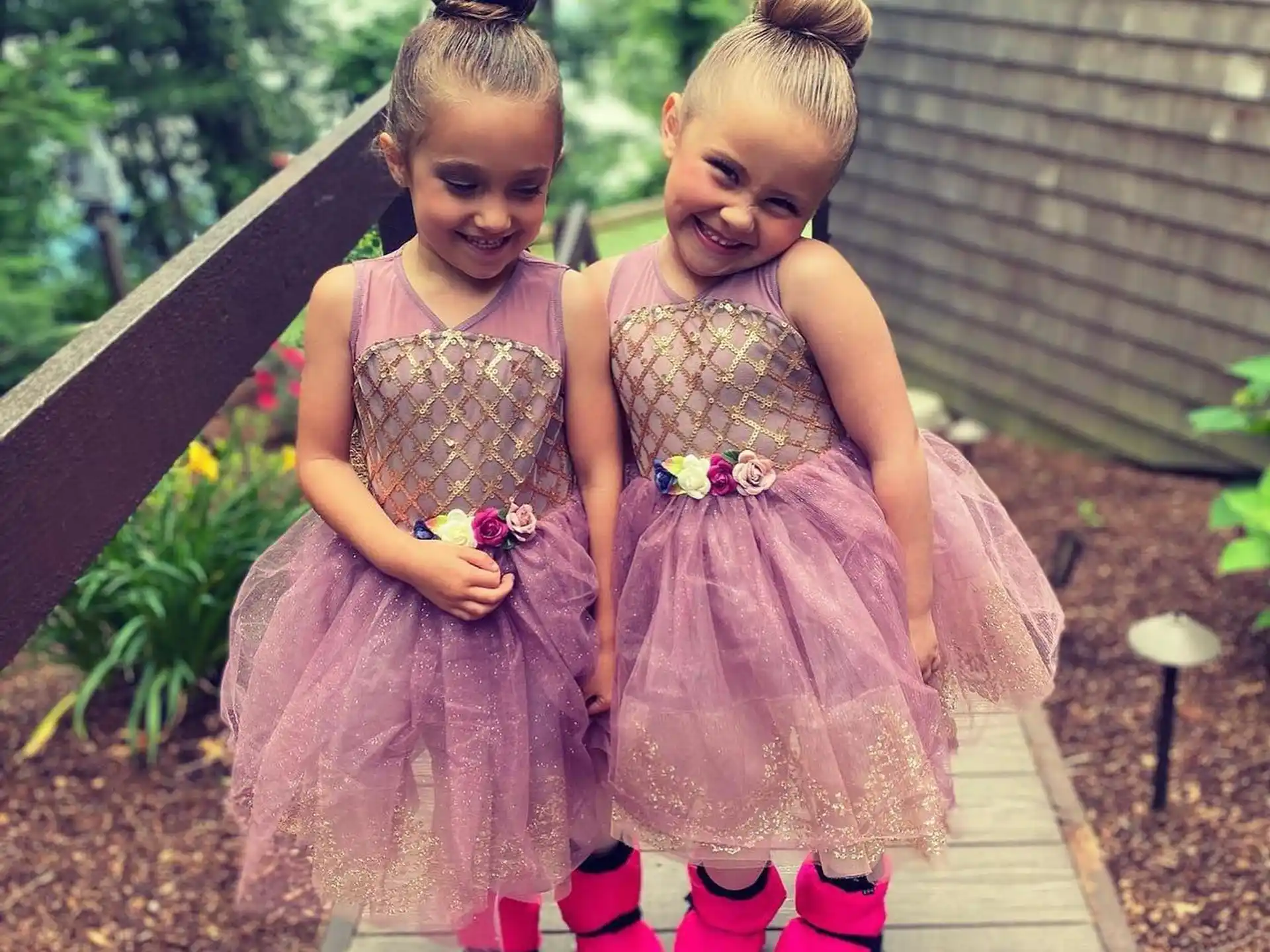 two girls wearing dresses and standing on a wood deck