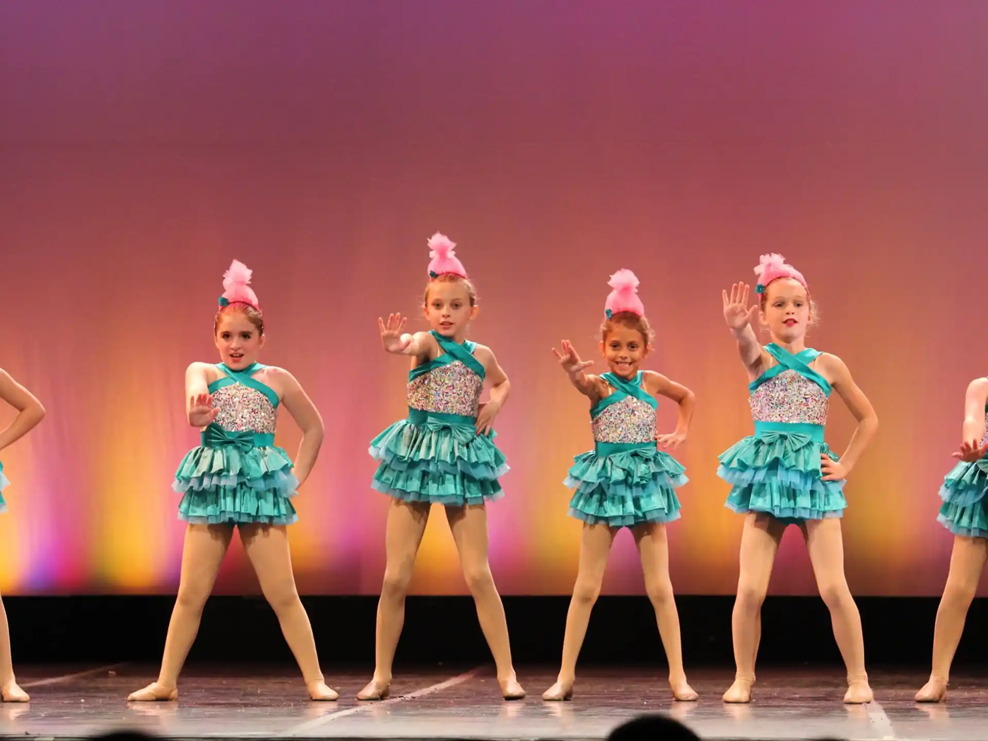 a group of girls wearing dresses and dancing on a stage