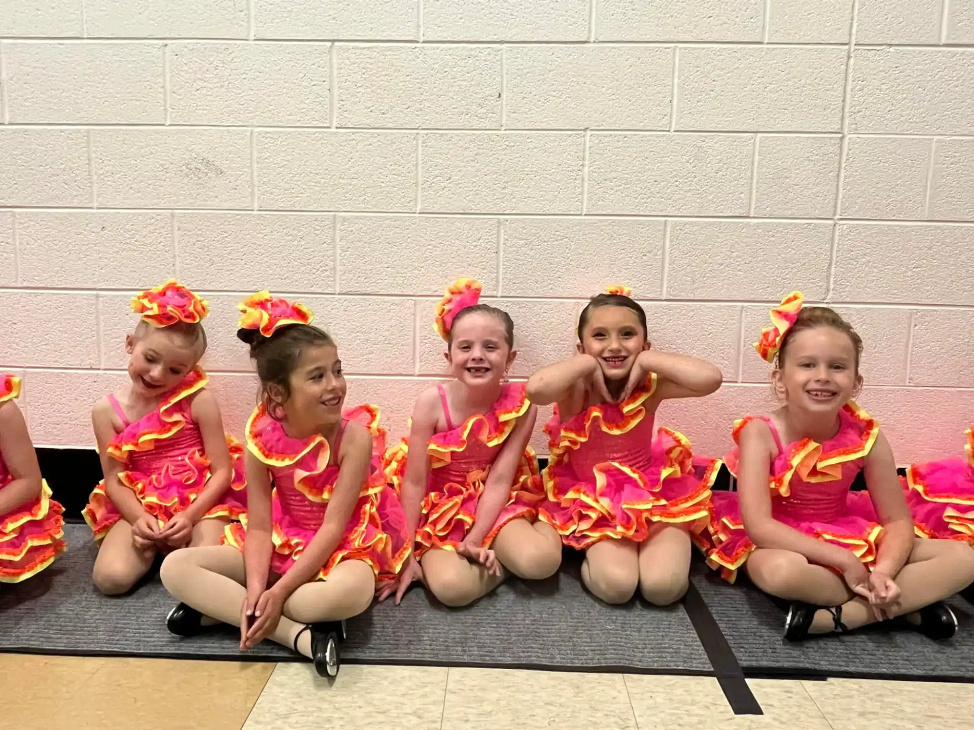 a group of girls wearing pink dresses and sitting on a bench