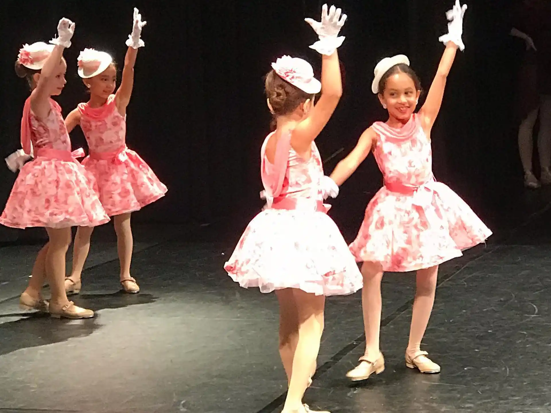 a group of girls wearing dresses and holding their hands up