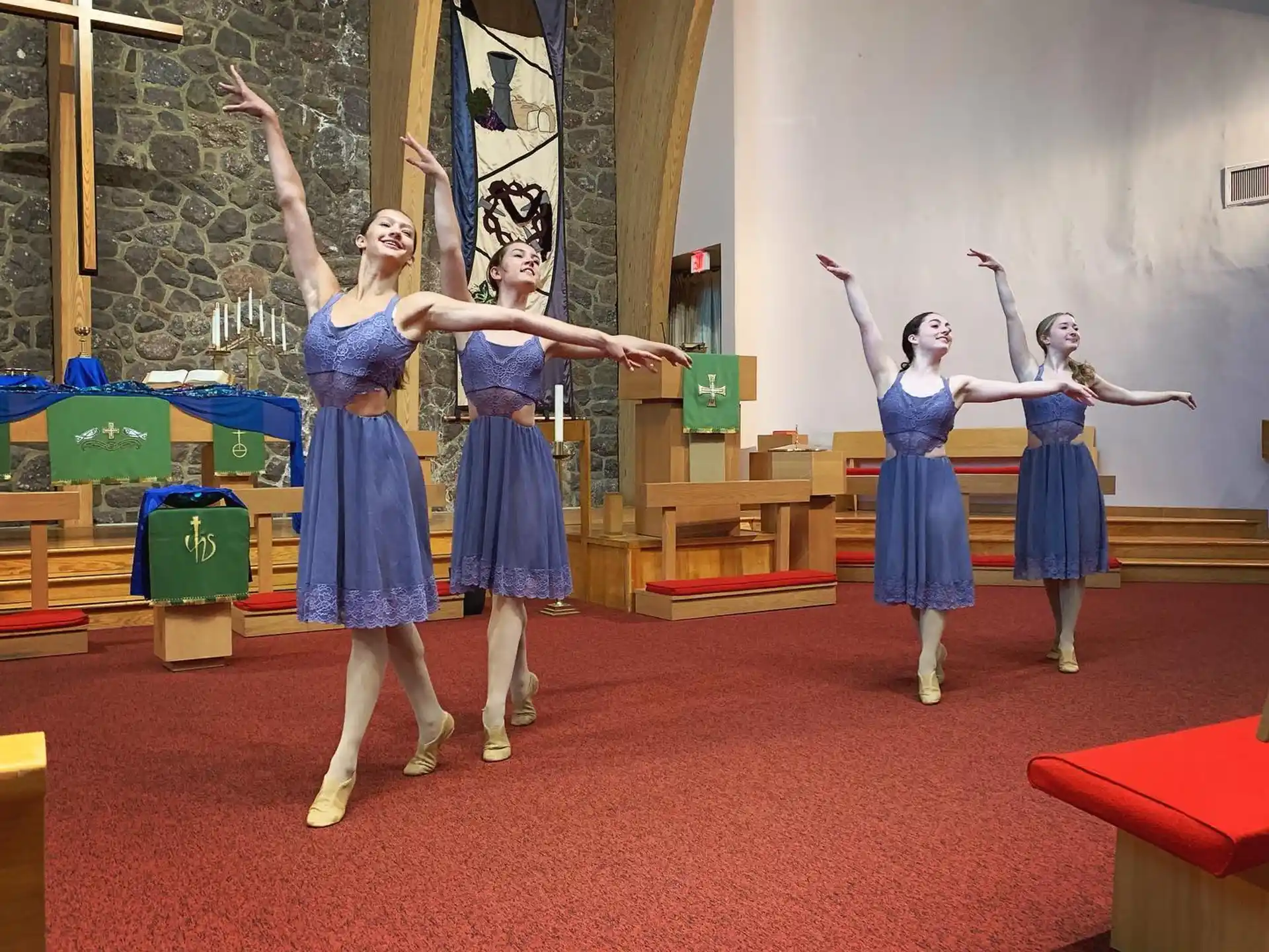a group of girls in blue dresses dancing in a room with a red carpet and a white wall