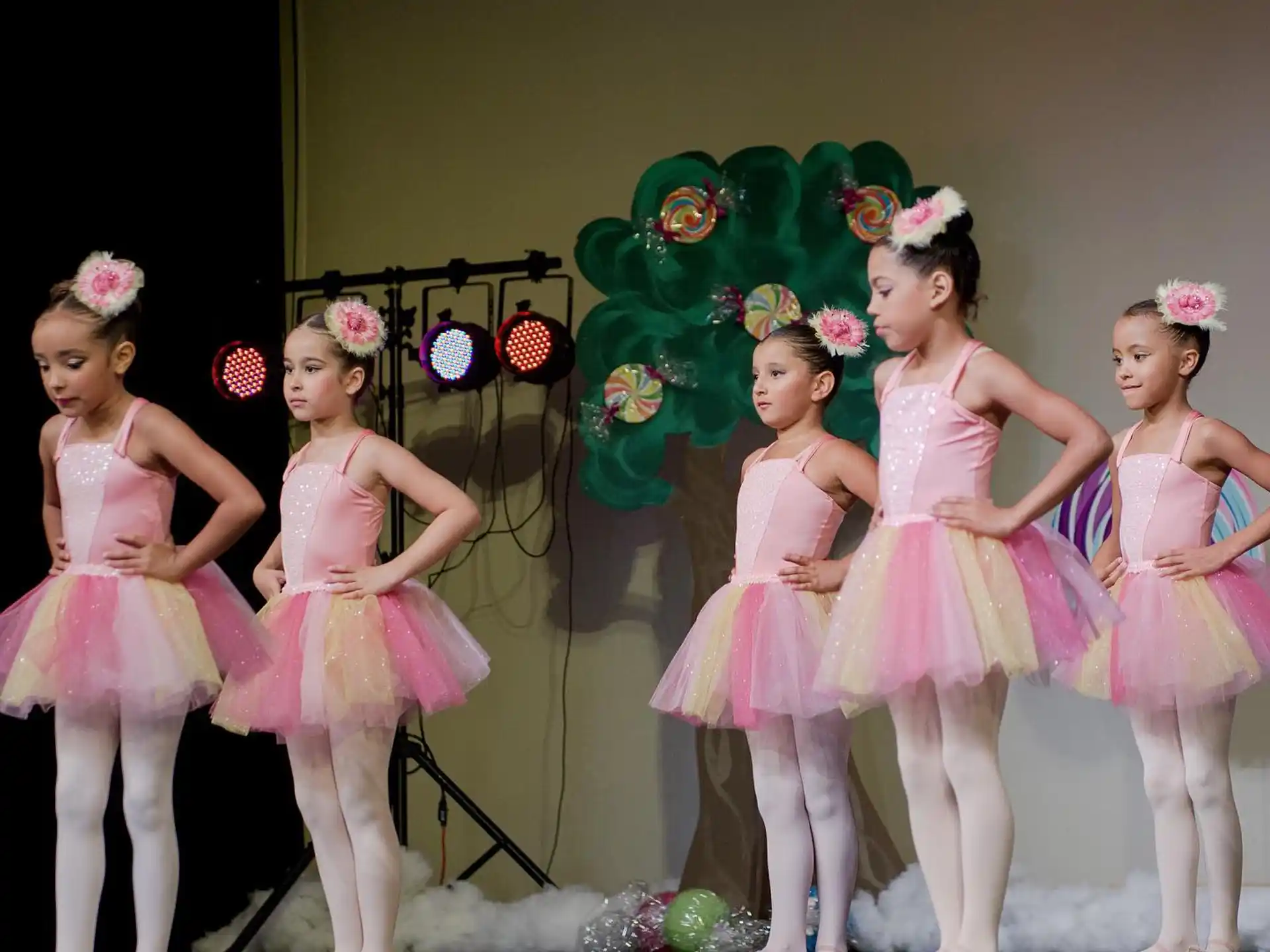 a group of girls in dresses and a green puppet on a stage