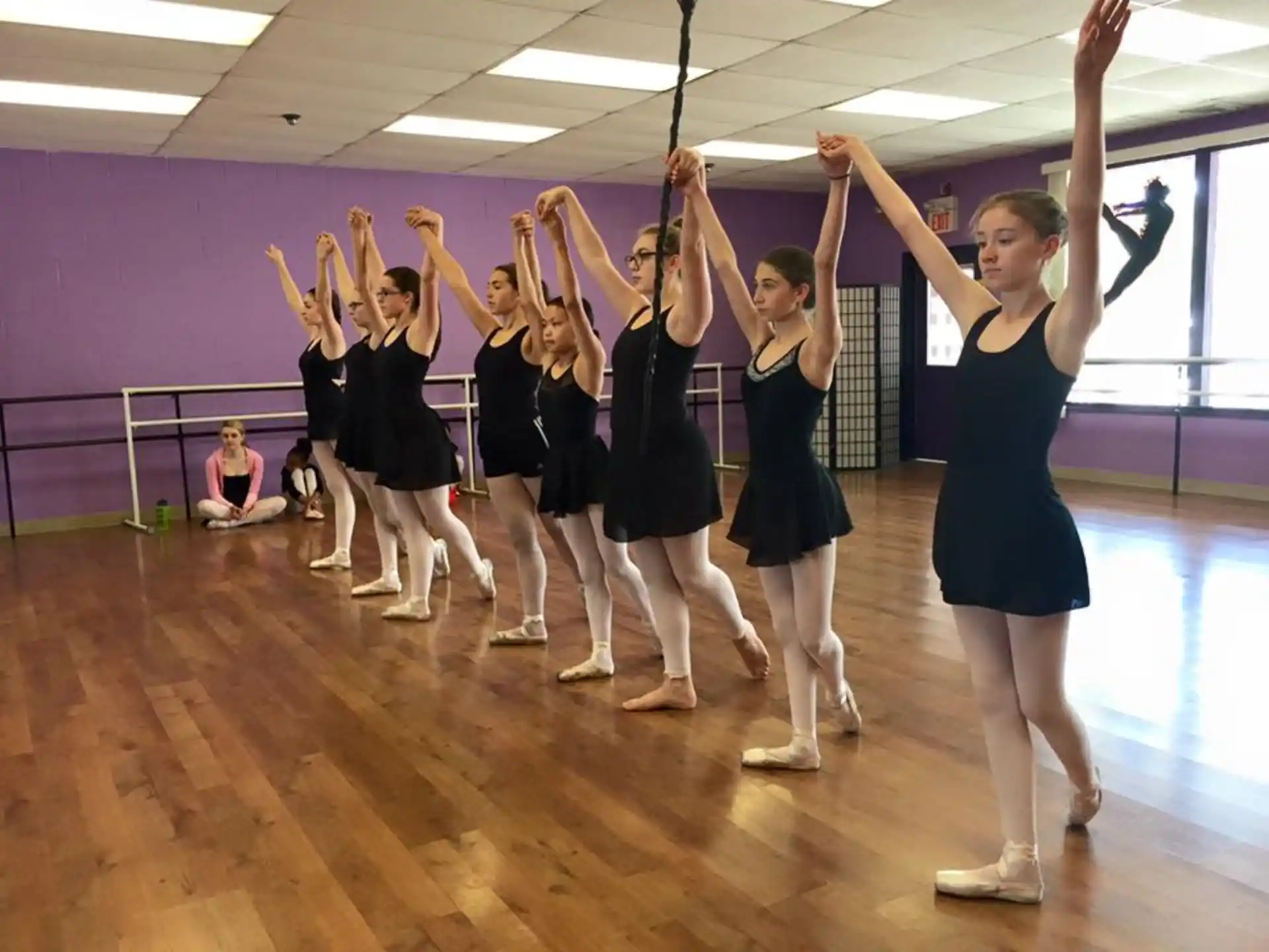 a group of girls in black dresses dancing on a wood floor