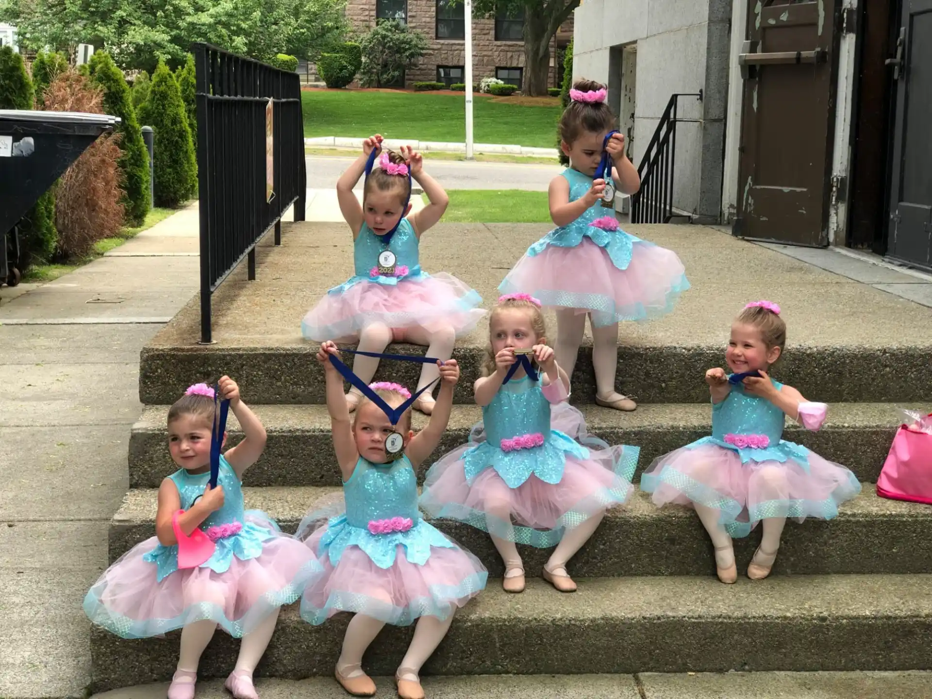 a group of girls in dresses and skirts sitting on a sidewalk