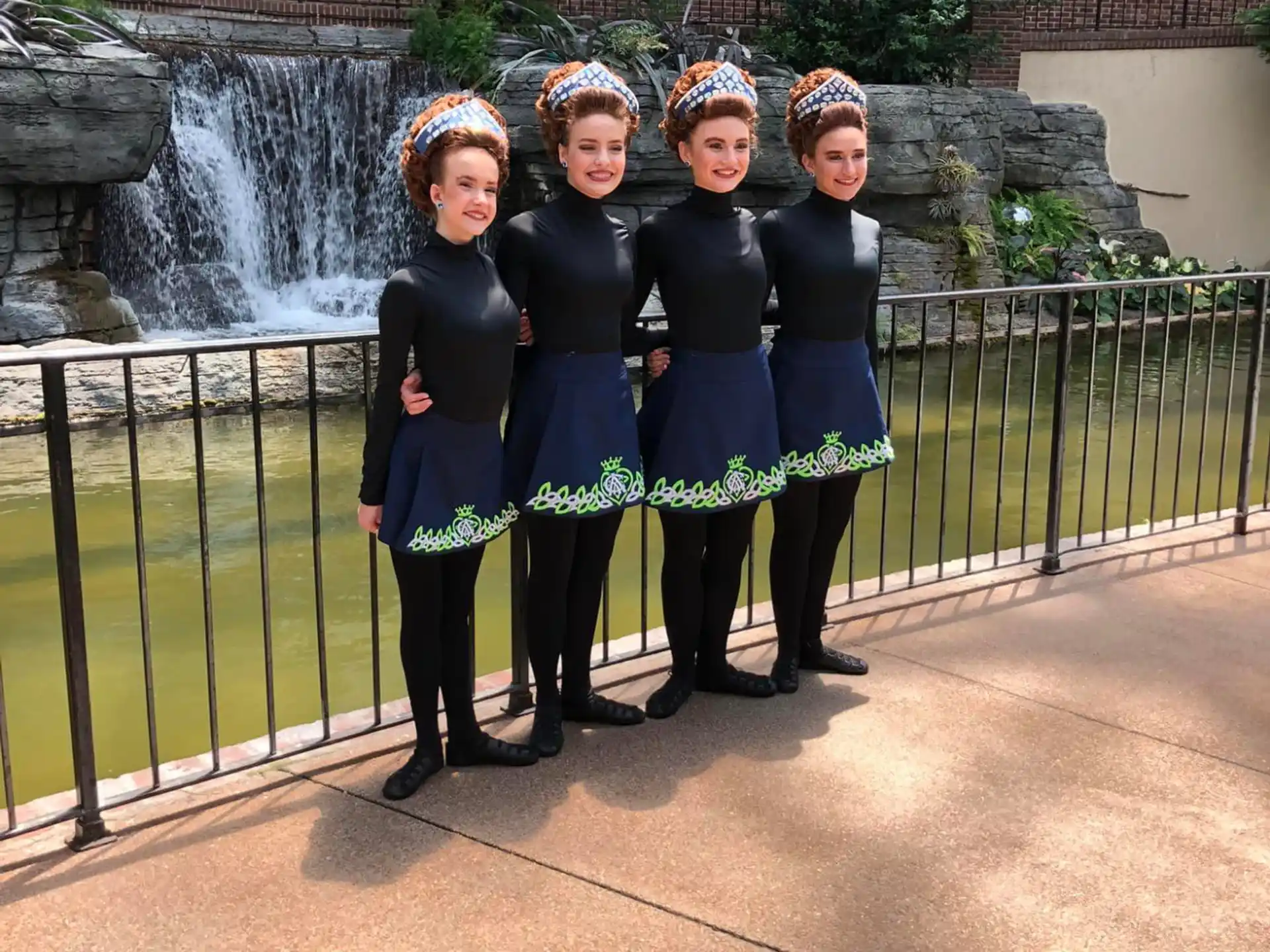 a group of girls in black and blue uniforms standing in front of a waterfall