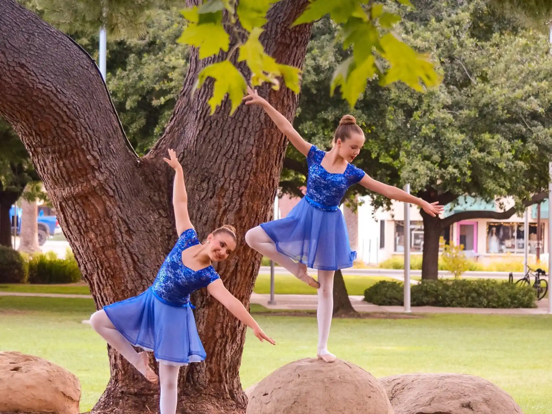 two women in blue dresses dancing under a tree