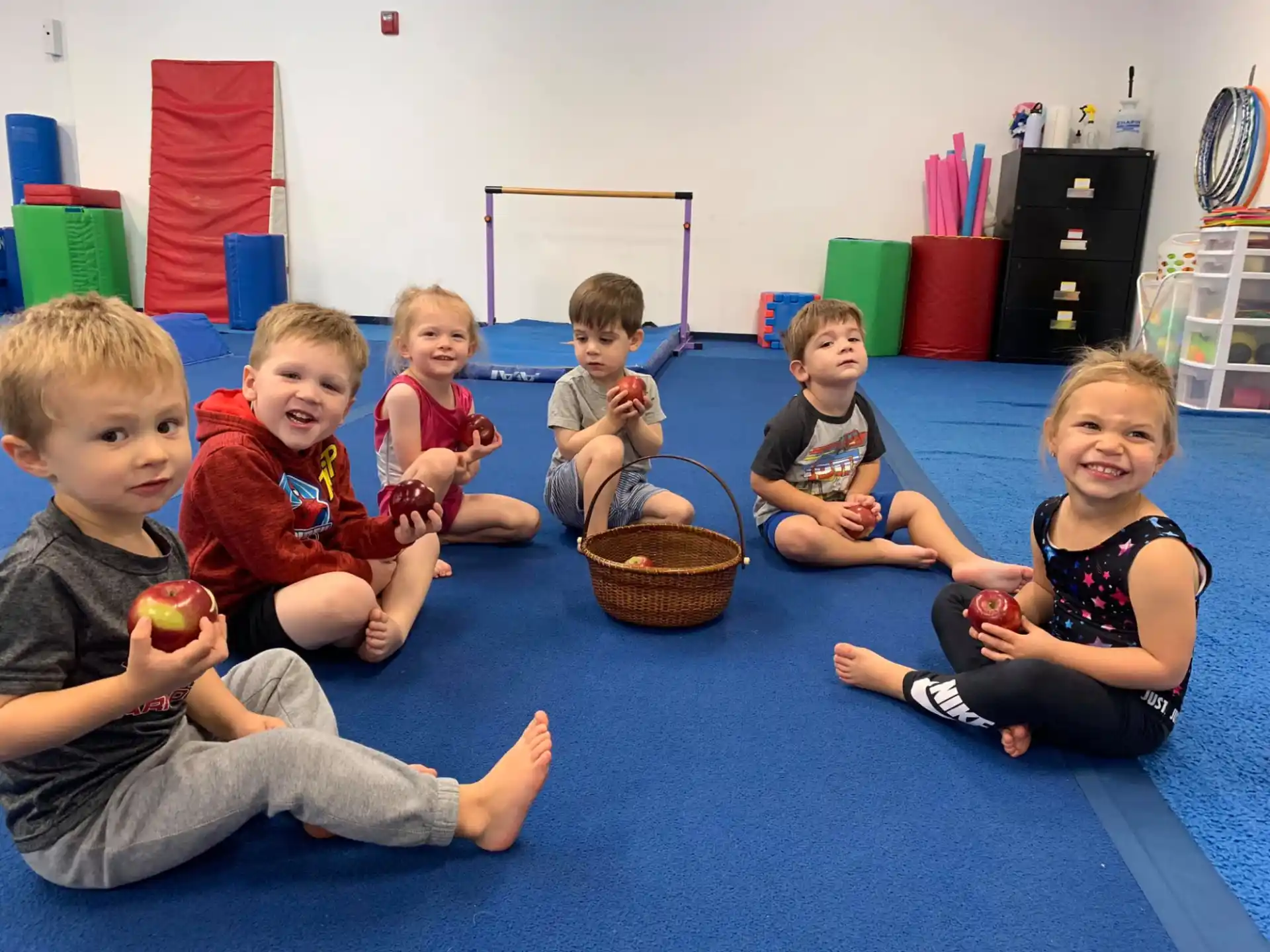 a group of children sitting on the floor eating apples