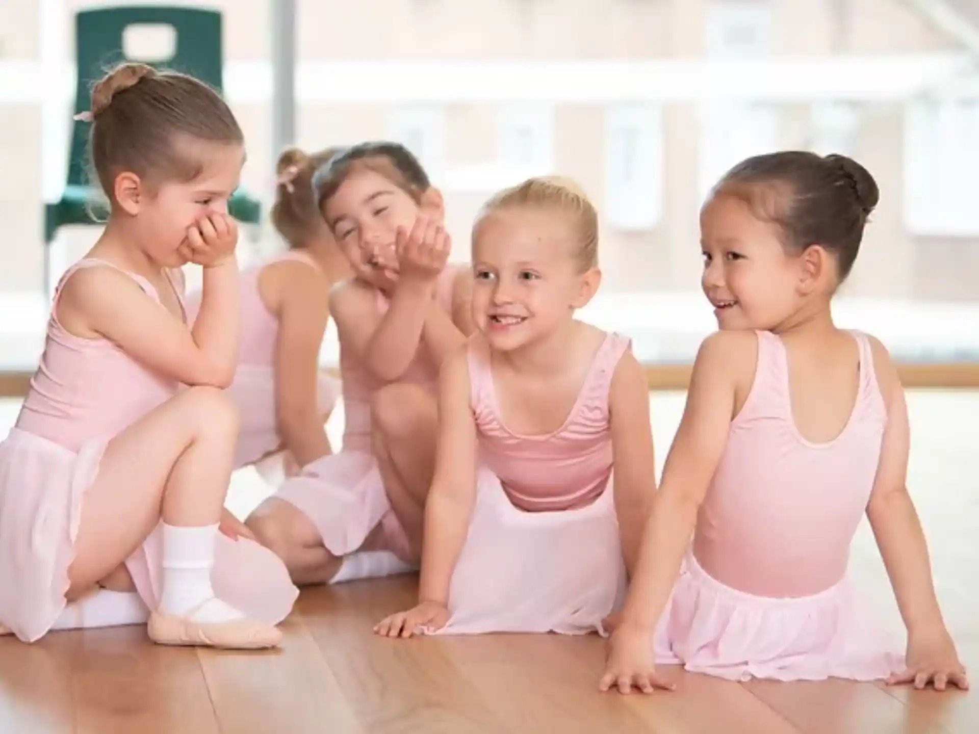 a group of young girls in pink dresses sitting on the floor