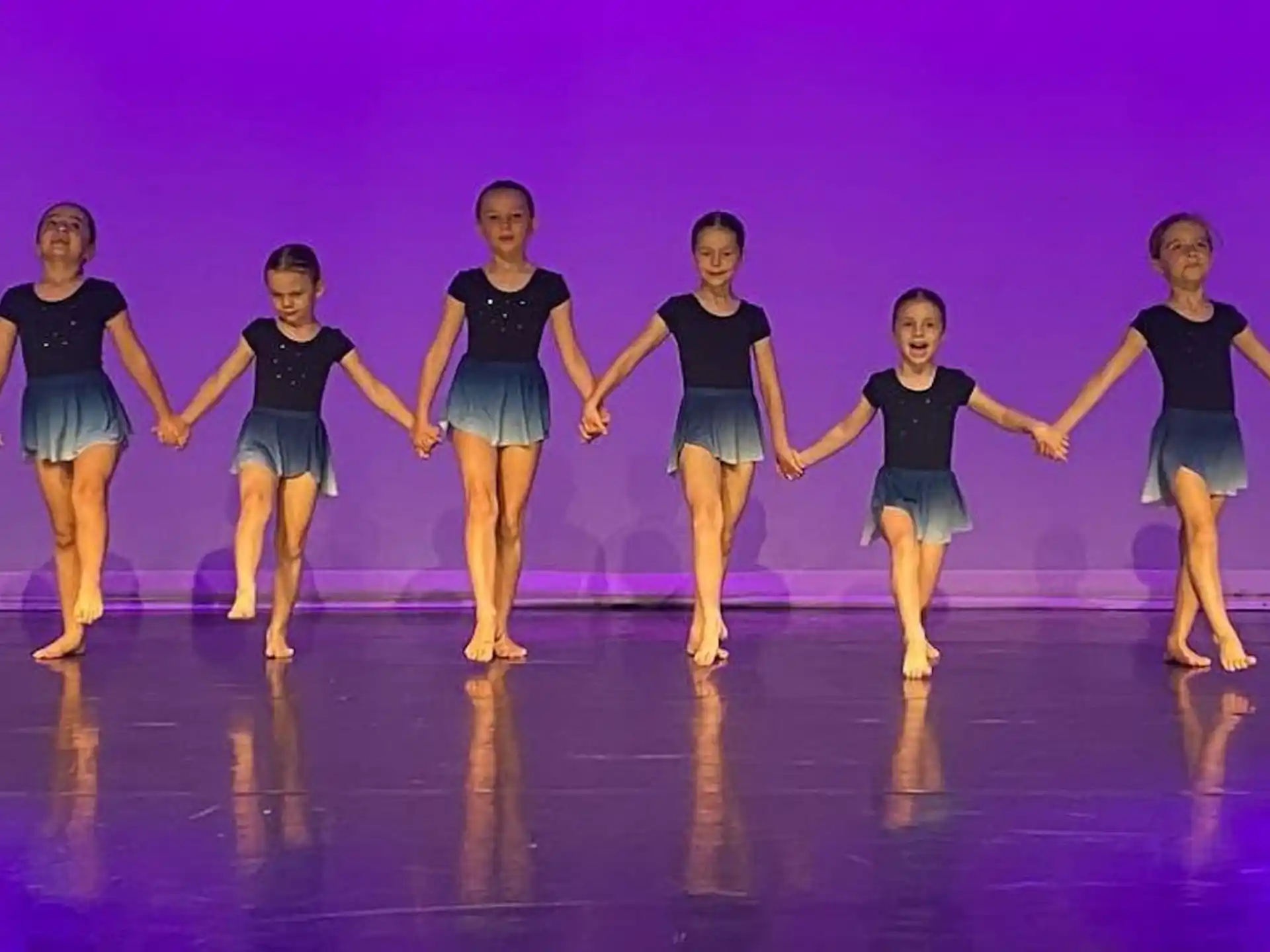 a group of girls in blue and black outfits jumping on a stage