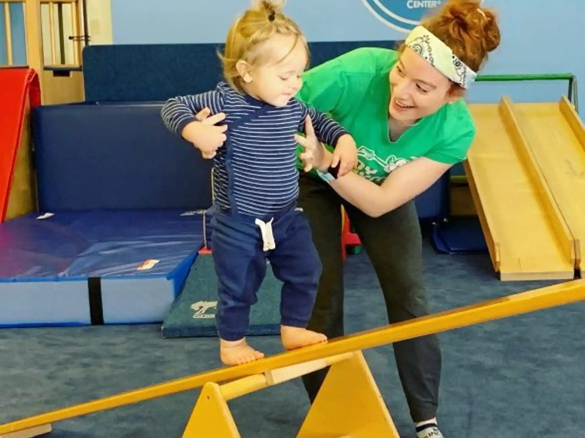 a couple of girls playing on a yellow mat in a room with blue chairs and a sign