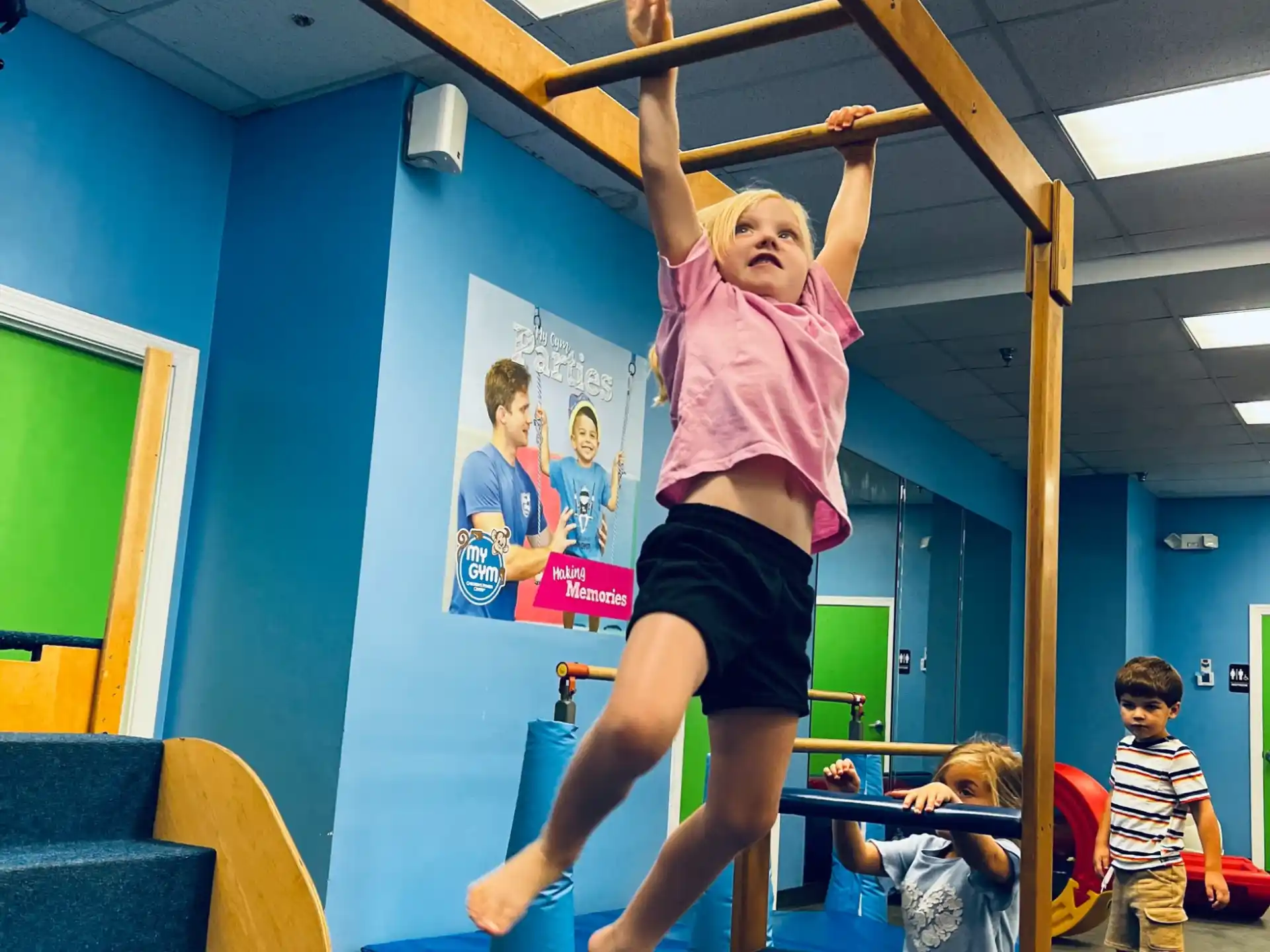 a girl doing a handstand on a pole in a room with other kids