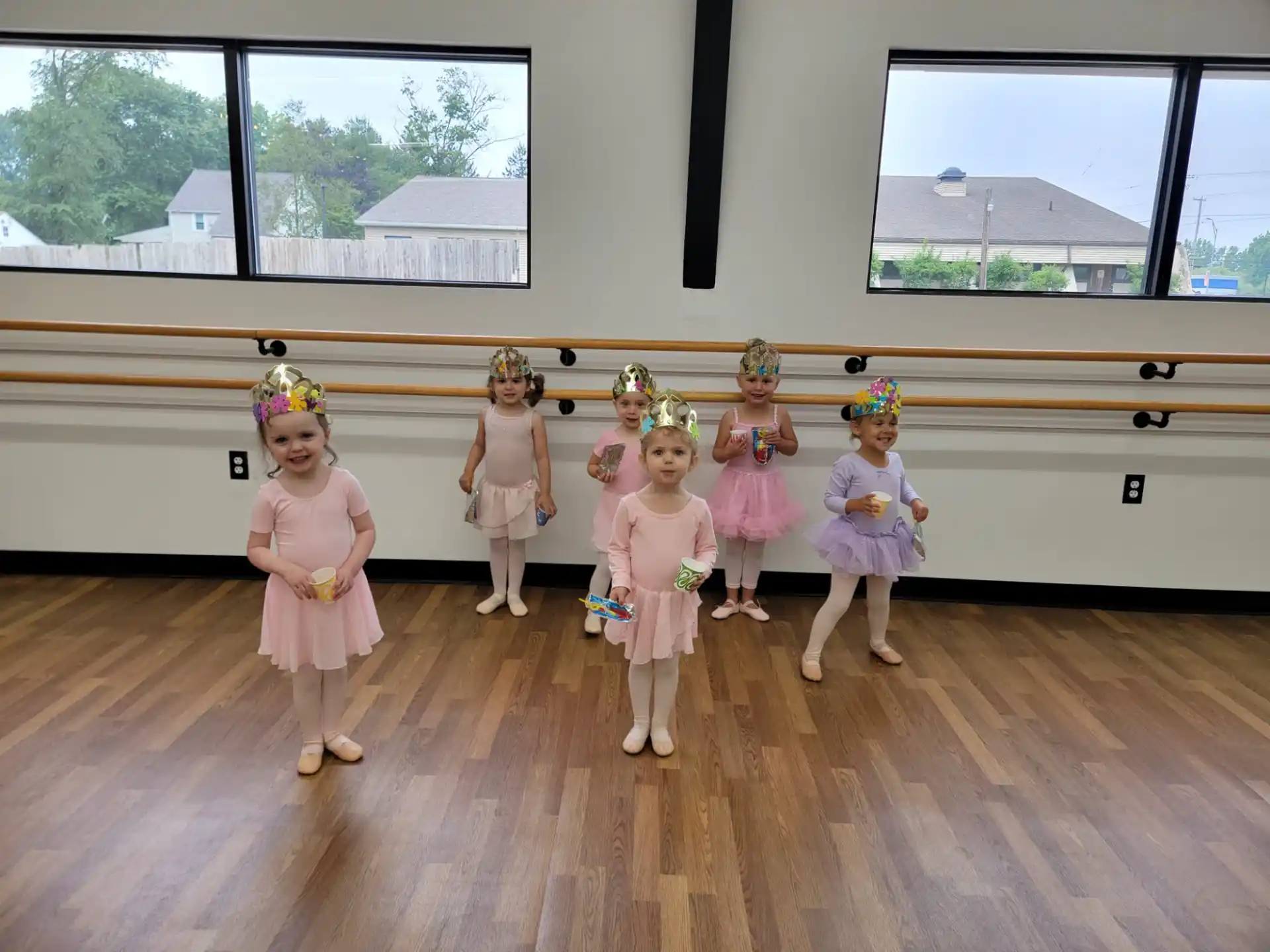 a group of girls in dresses and hats standing on a wood floor