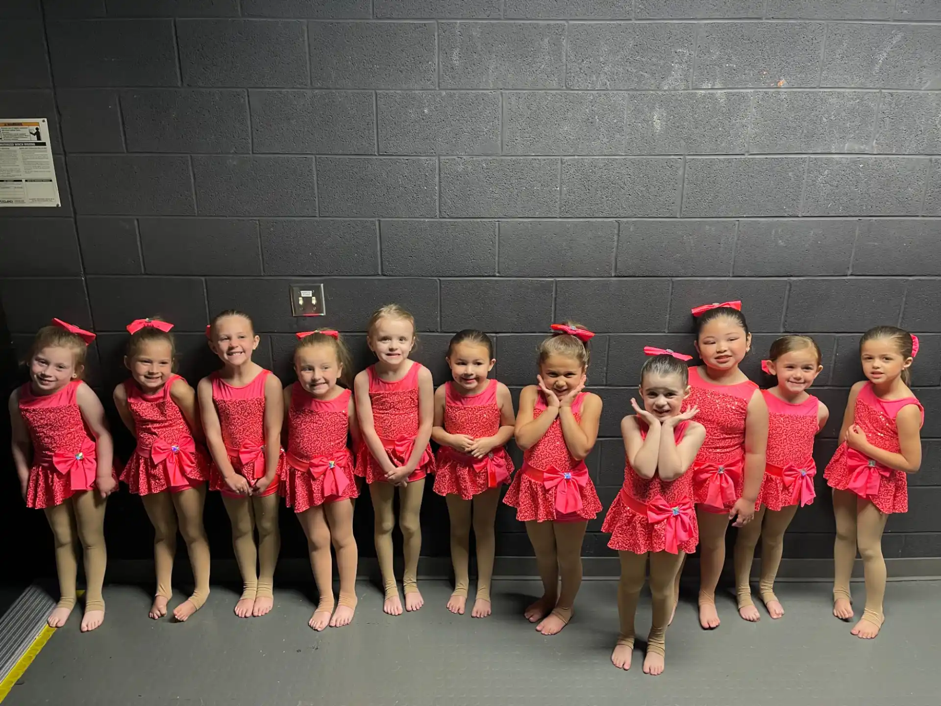 a group of children in red and white dresses standing in front of a black wall