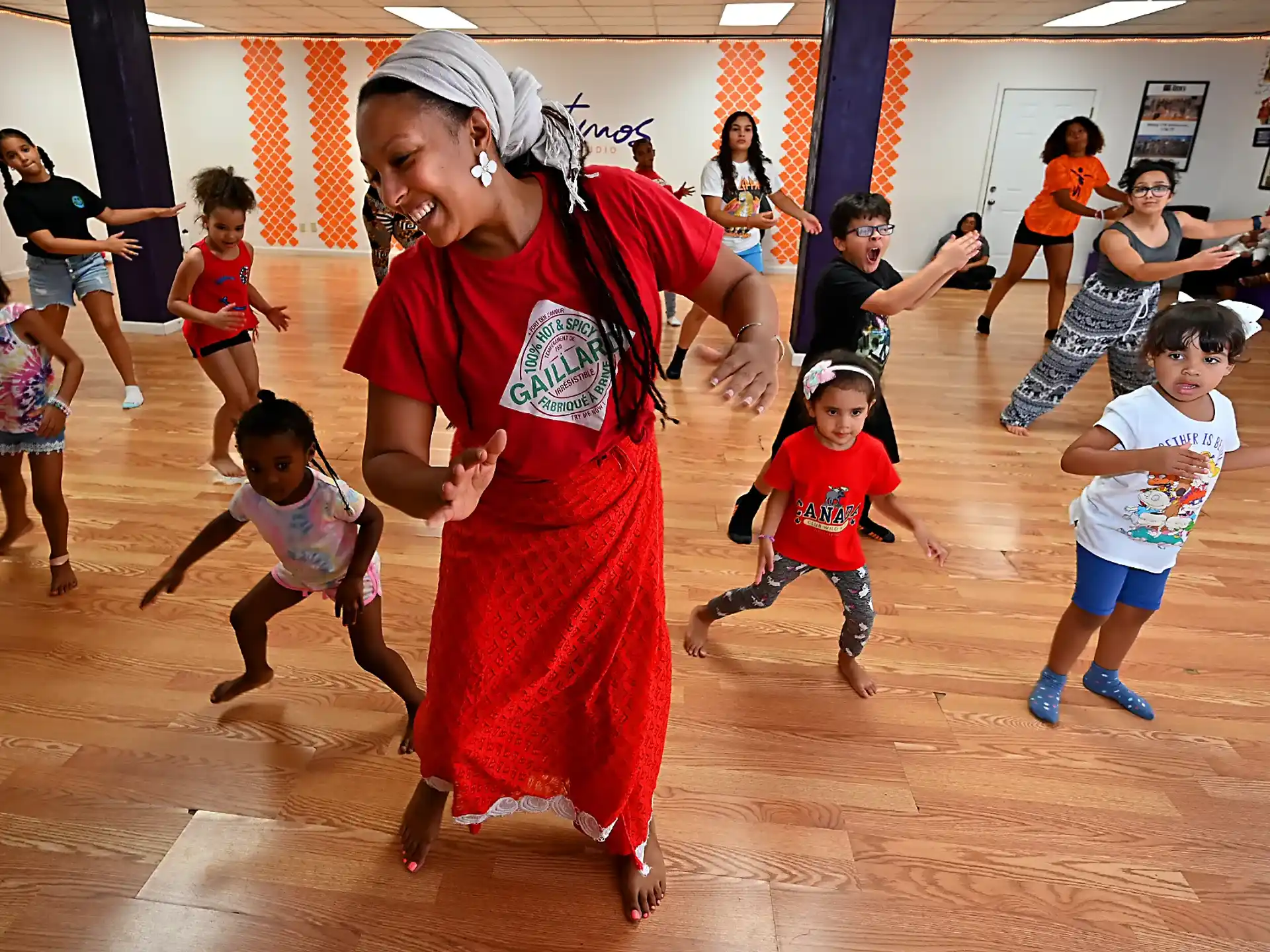 a person in a red dress dancing with kids in a gym