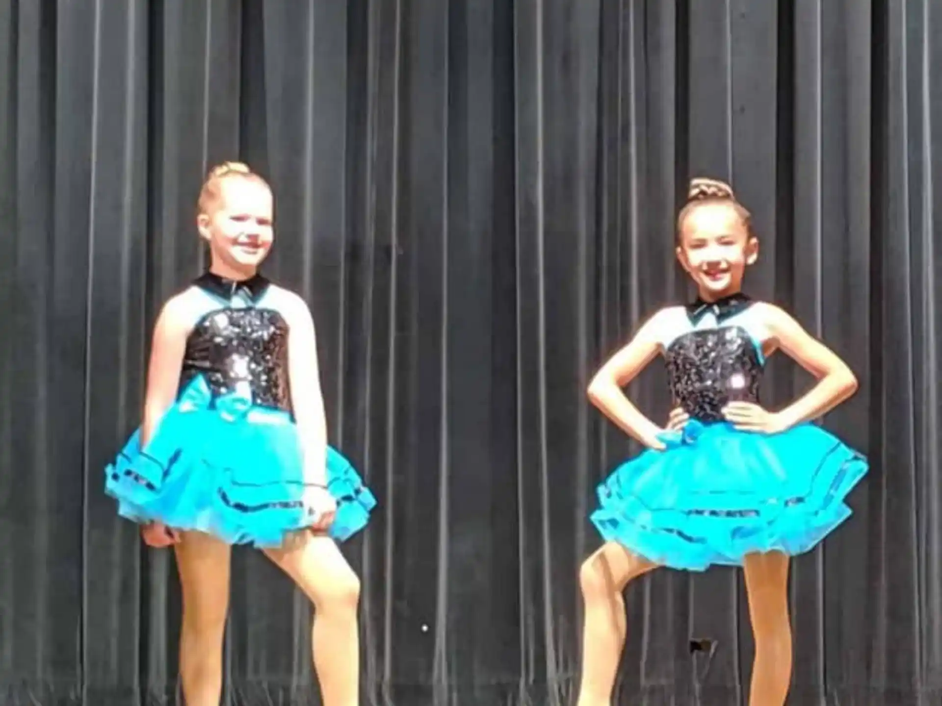 a couple of girls wearing dresses and dancing on a stage