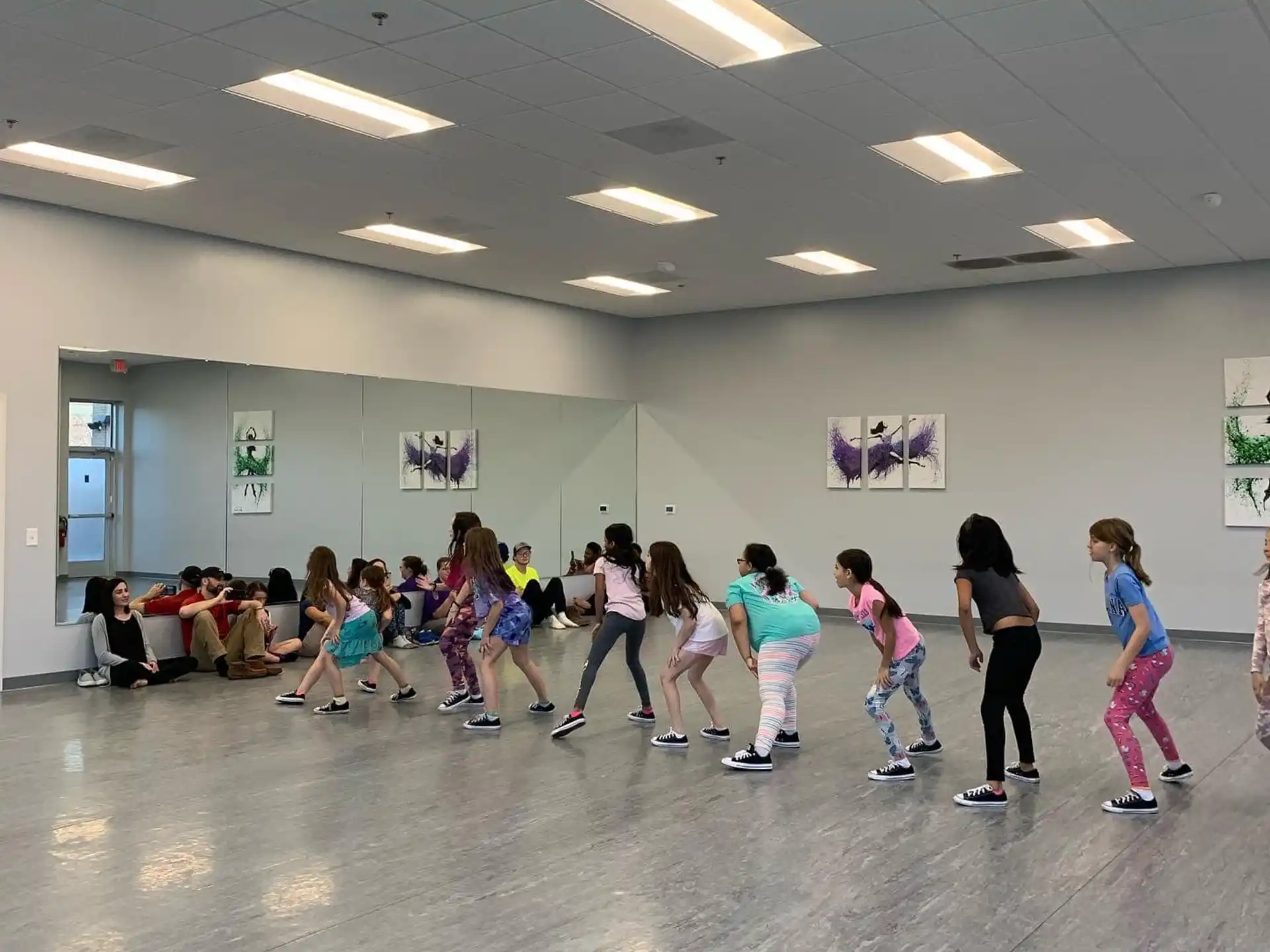 a group of people dancing in a room with a white wall and a wood floor