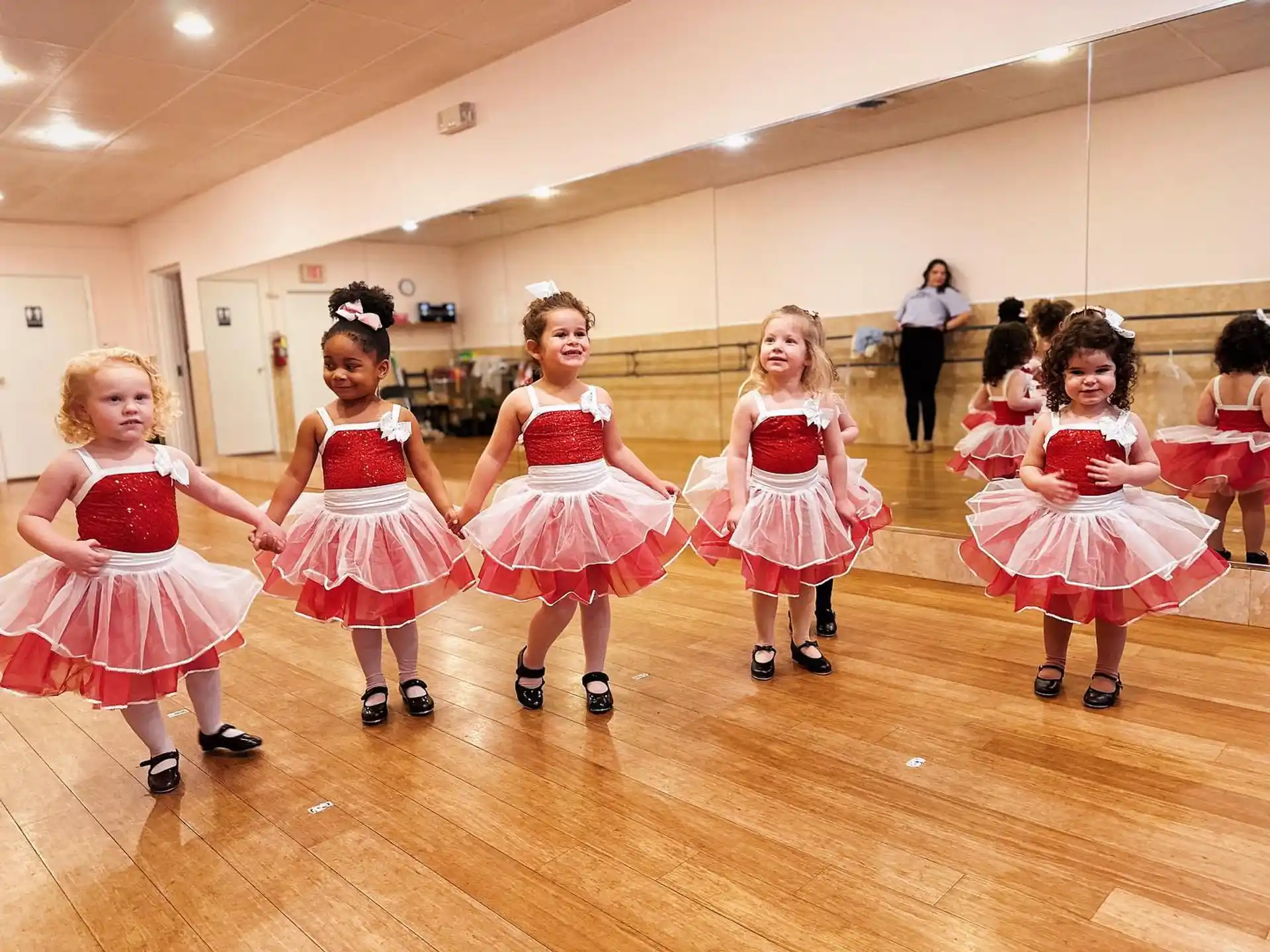 a group of girls in dresses and skirts dancing on a wood floor