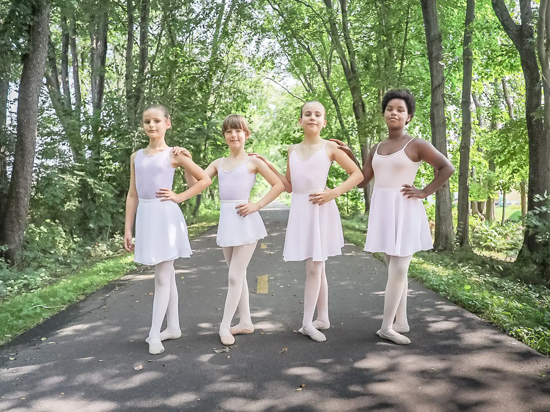 a group of girls in white dresses walking down a path in the woods