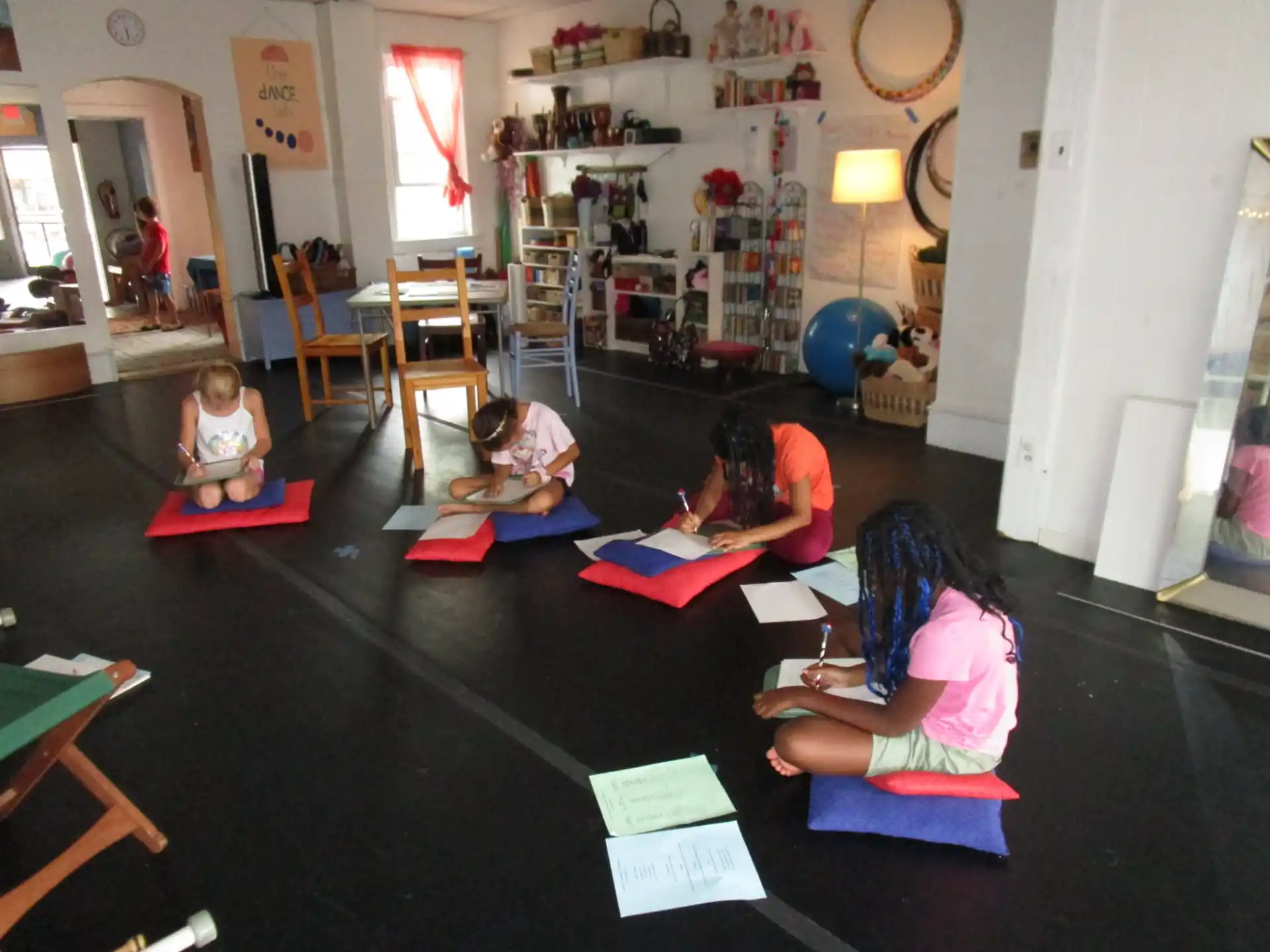 a group of children sitting on mats in a room with a table and chairs