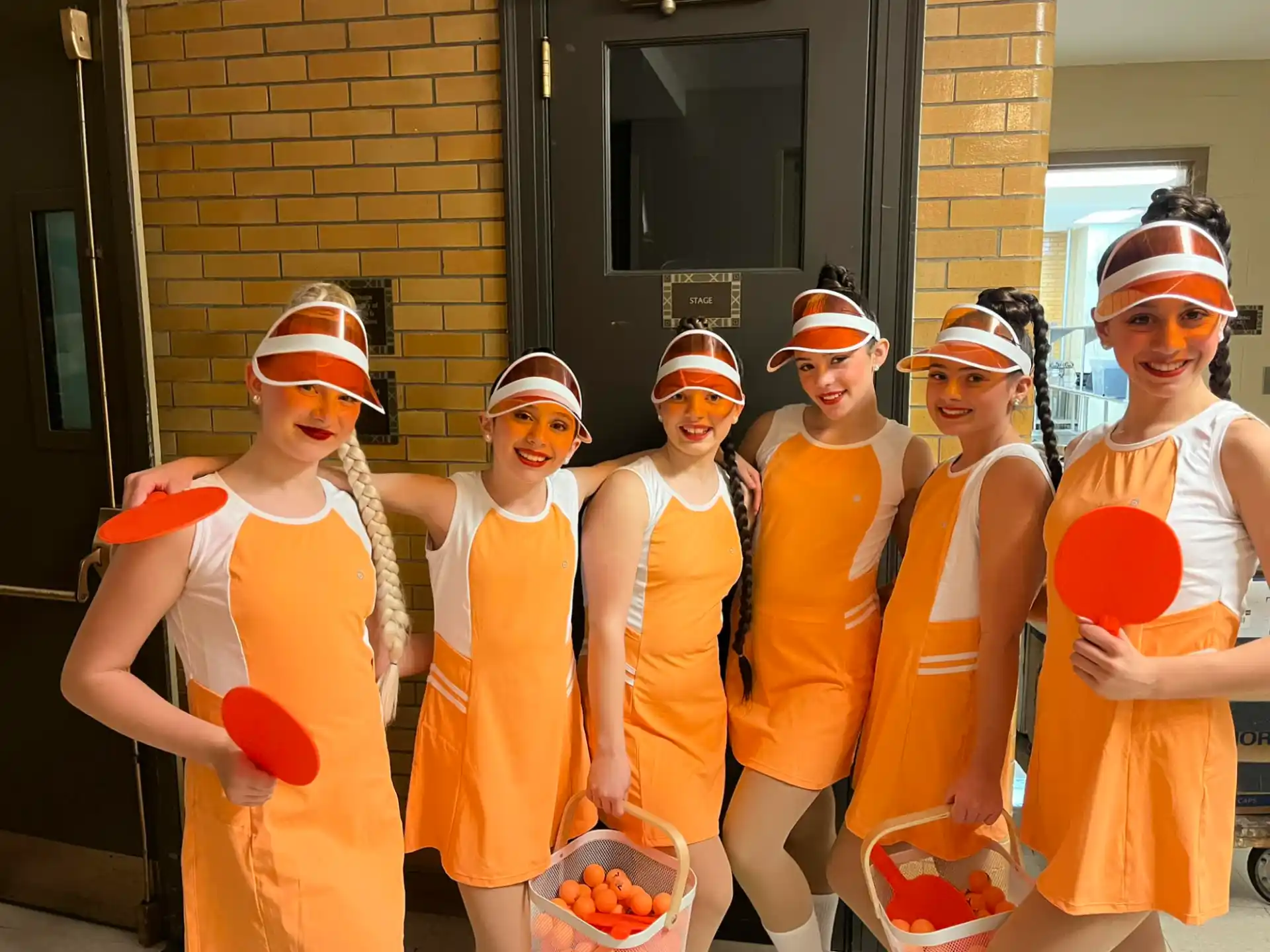 a group of women wearing orange dresses and holding buckets