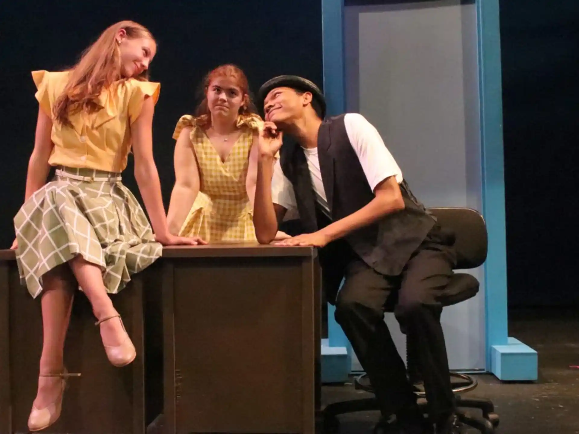 a person sitting on a stool with a group of women standing behind him