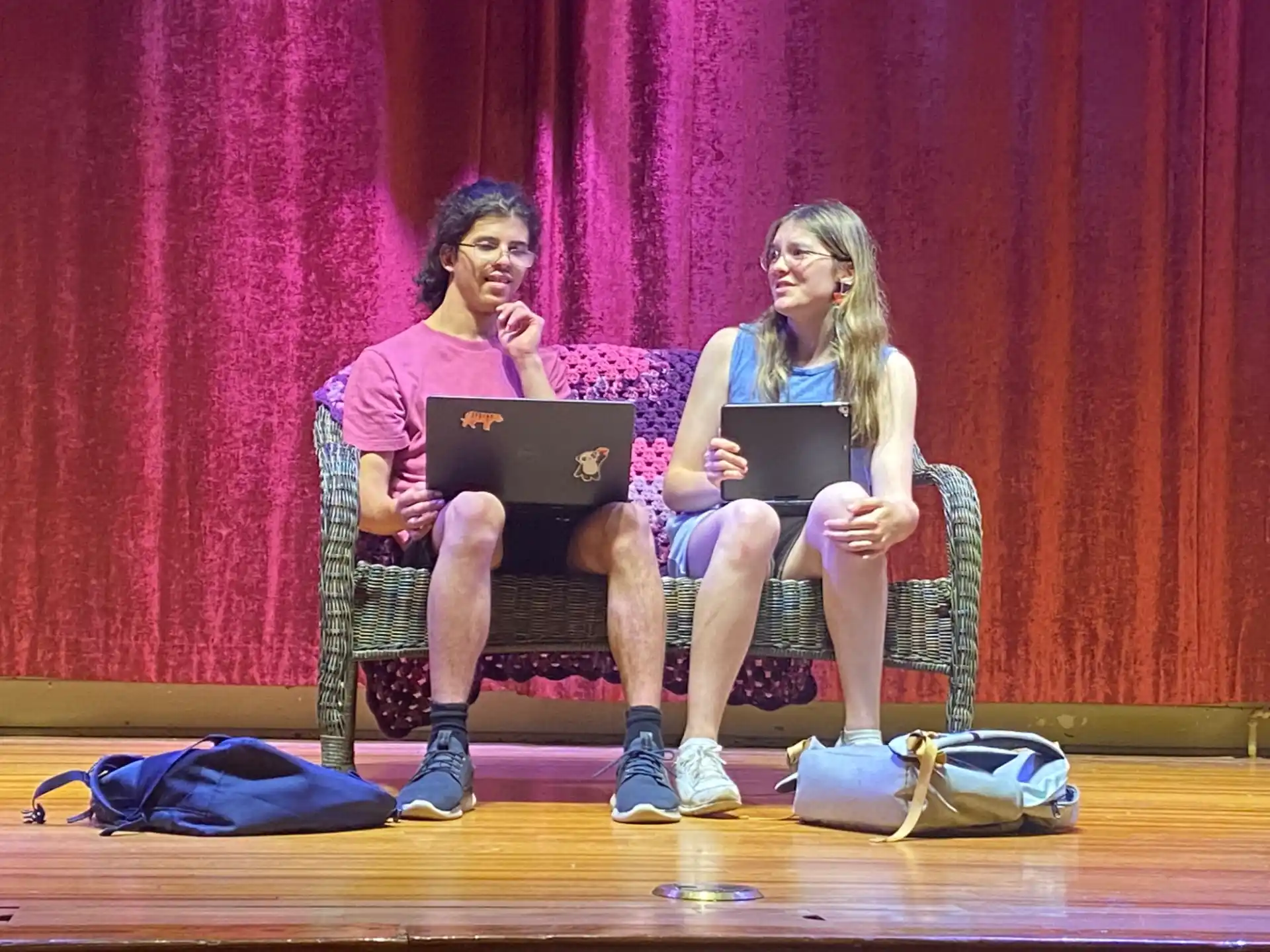 a man and a woman sitting on a bench with laptops