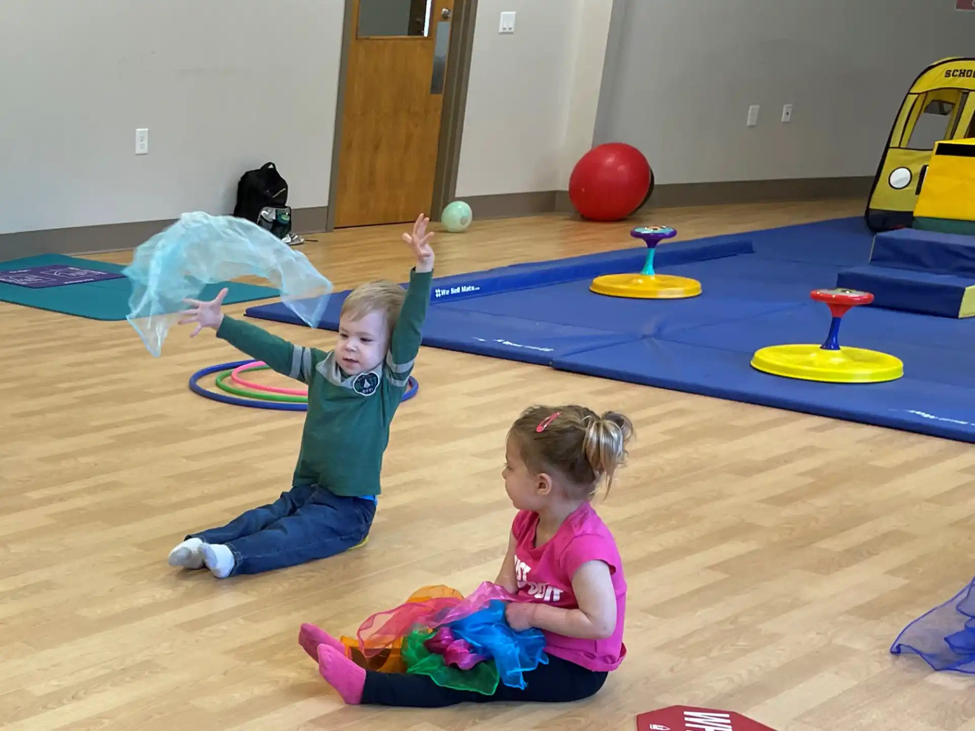 a couple of children playing on a blue mat in a room with a blue table and yellow balls