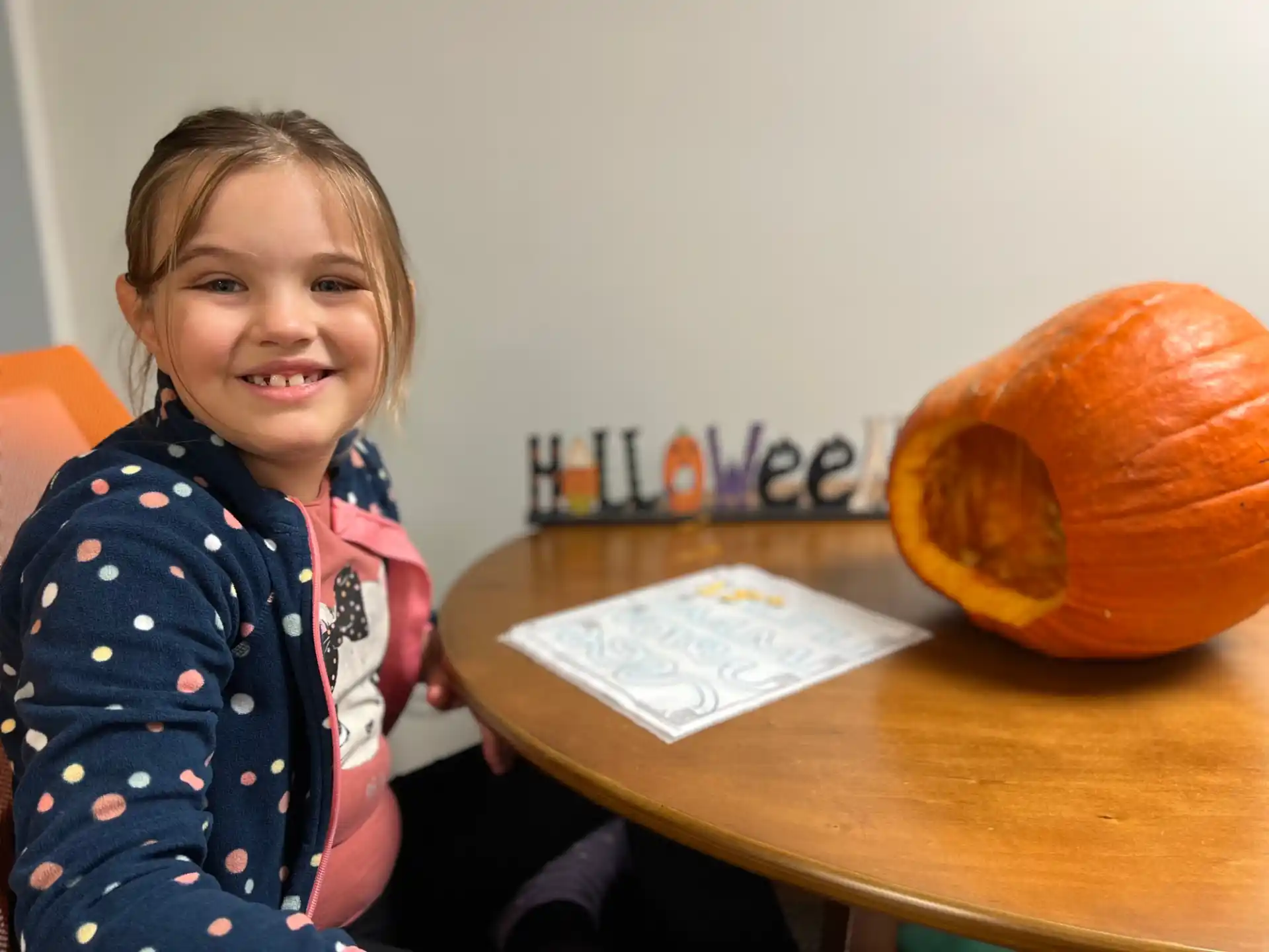 a girl sitting at a table with a pumpkin and a book