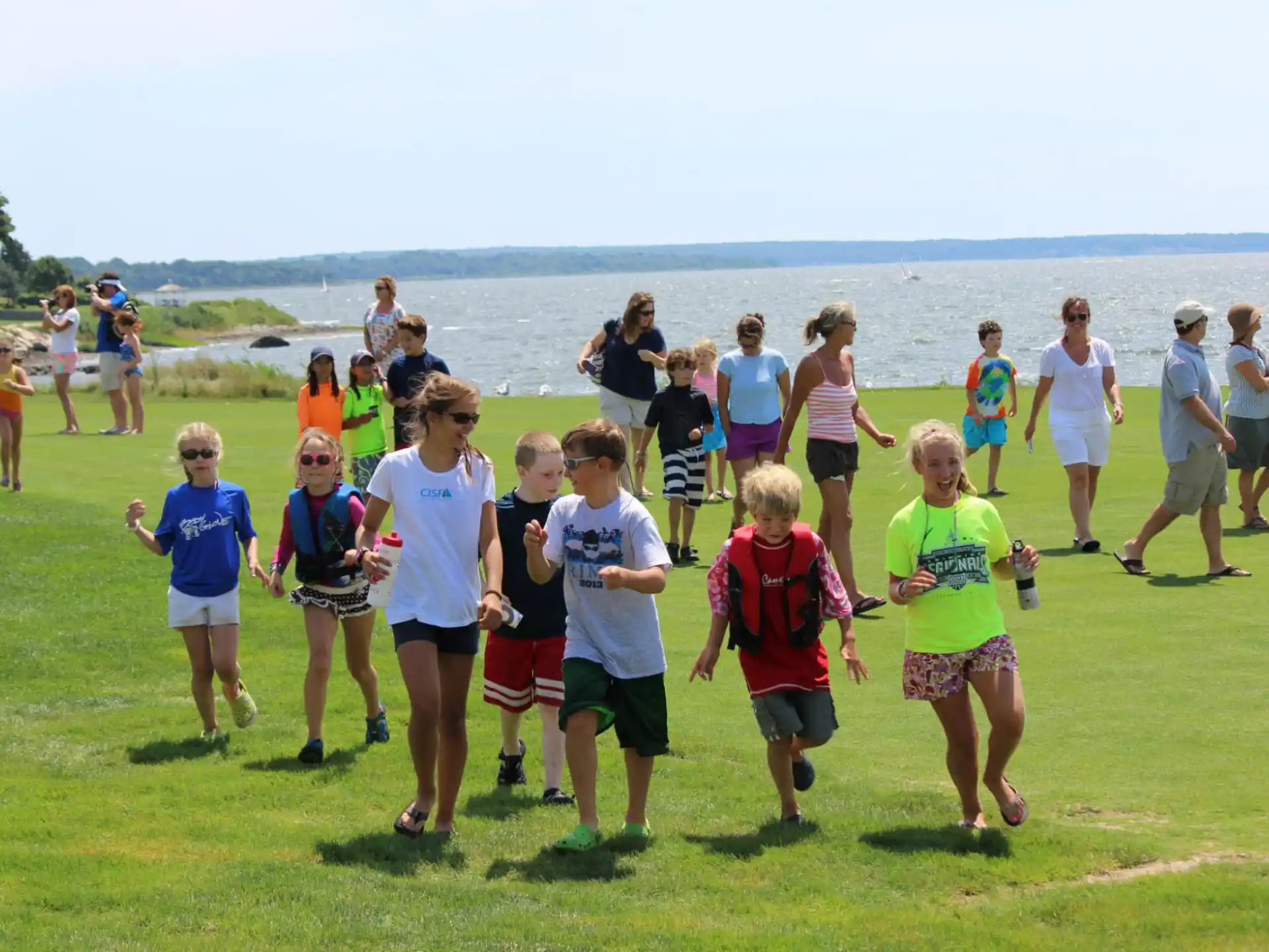a group of people standing on grass by a body of water