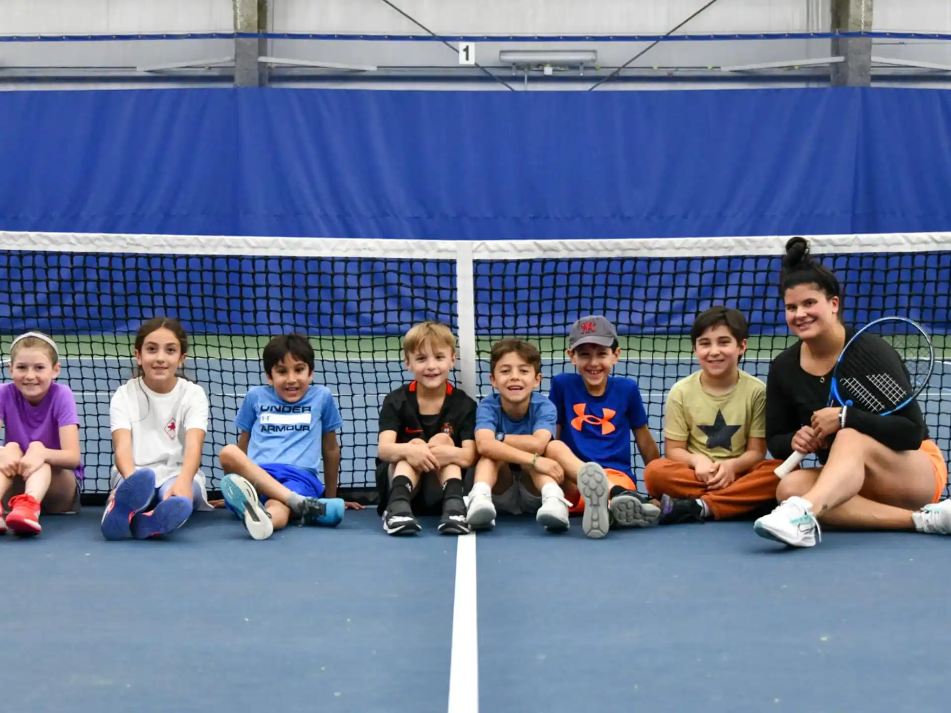 a group of kids sitting on the ground with a tennis racket