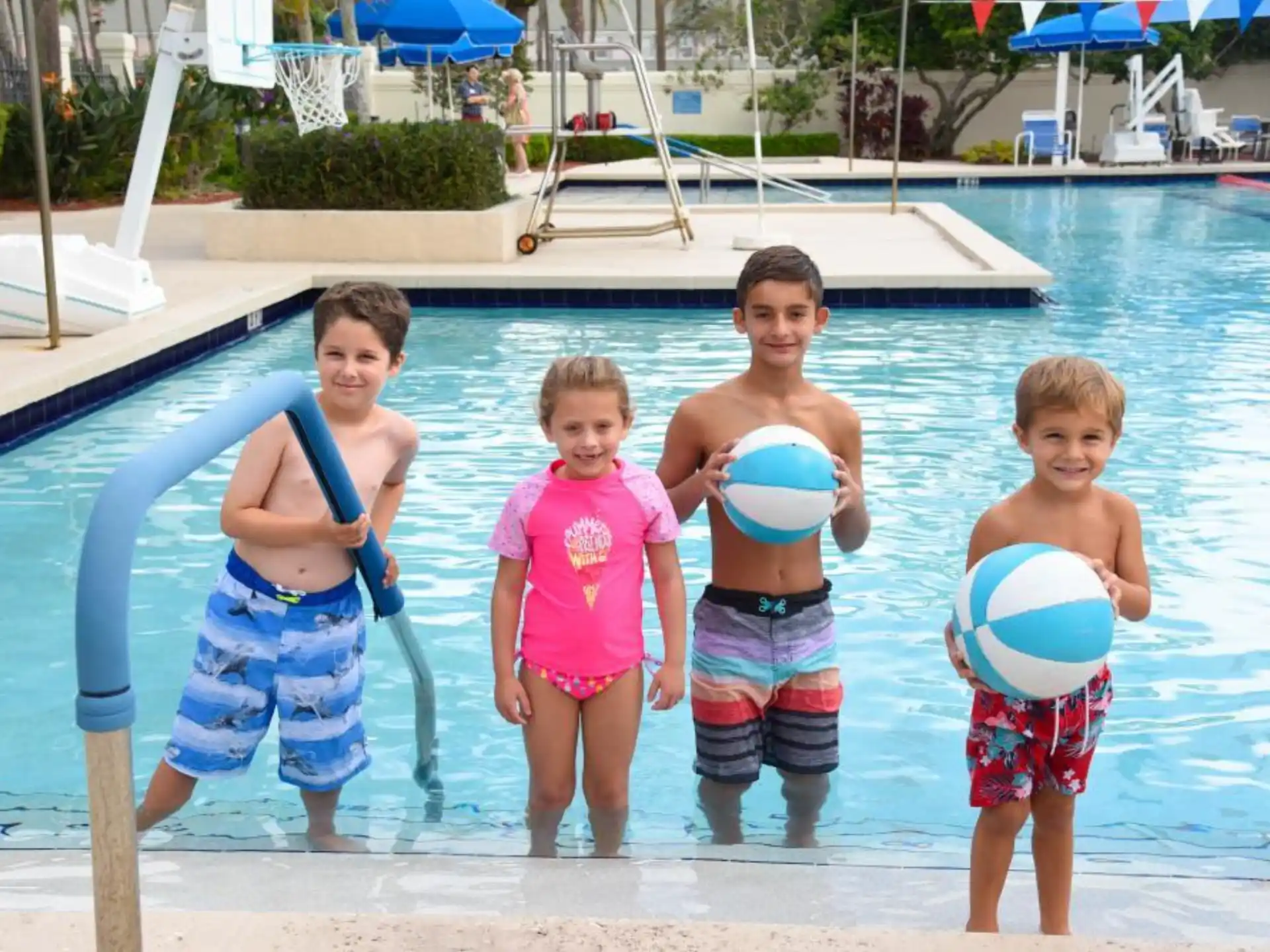 a group of kids holding blue and white balls in front of a pool