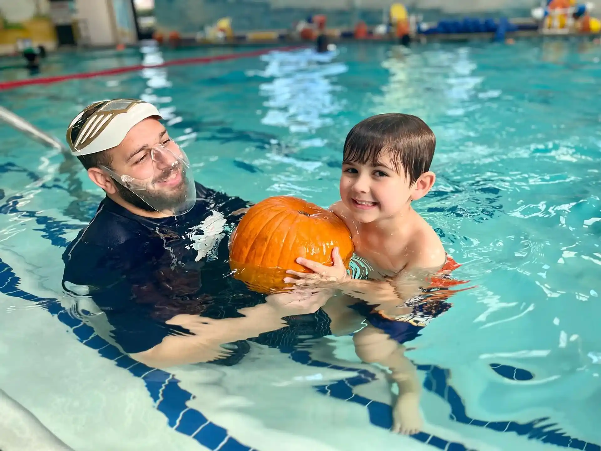 a person and a boy in a pool with an orange ball