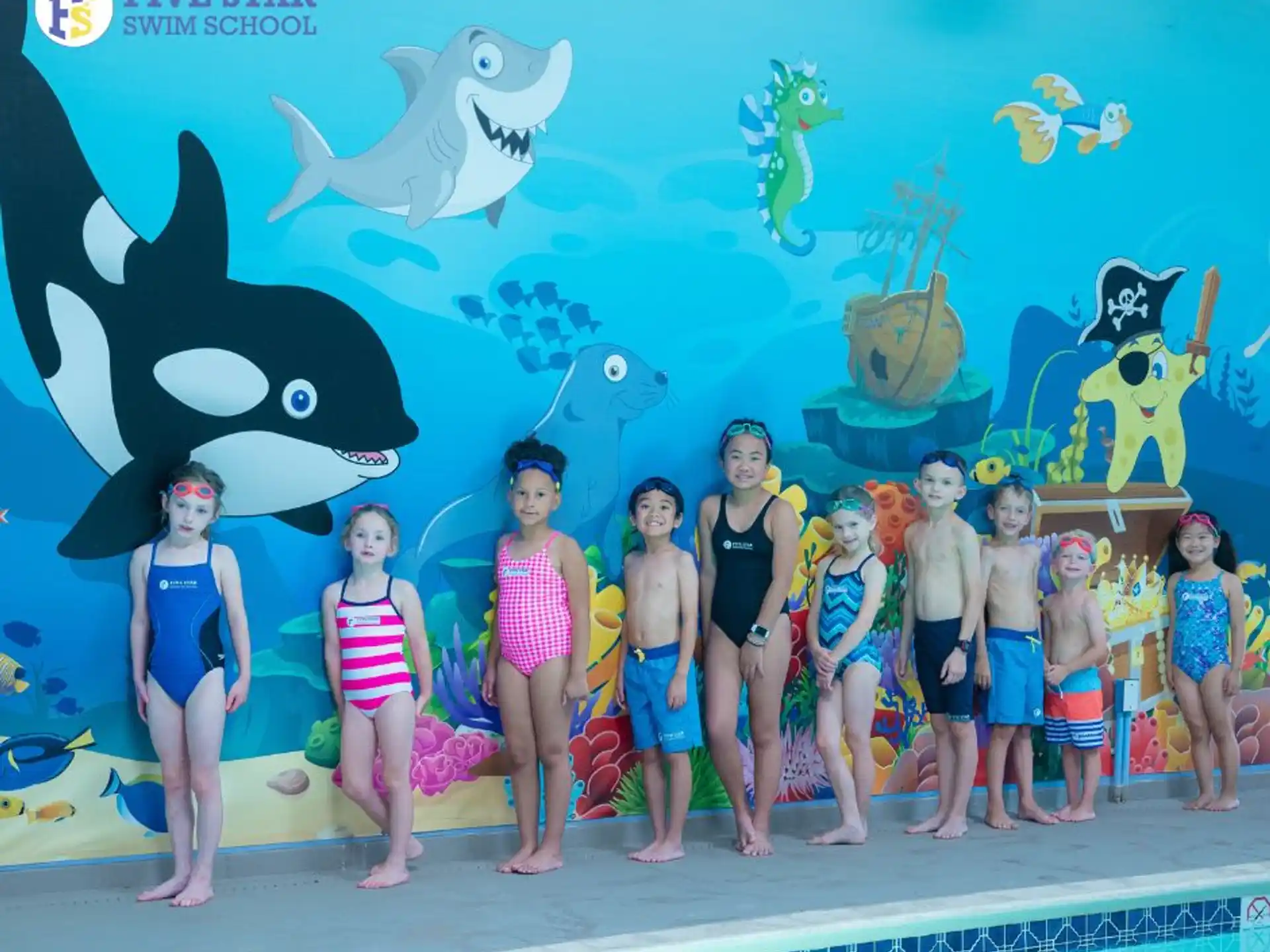 a group of people posing for a photo in front of a large blue wall with fish