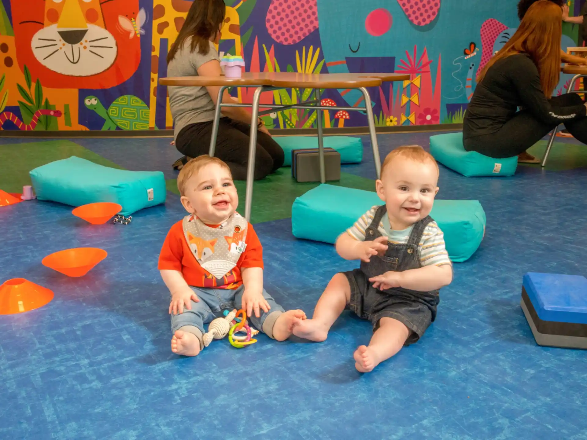a couple of young children sitting on the floor in a room with a table and chairs and a