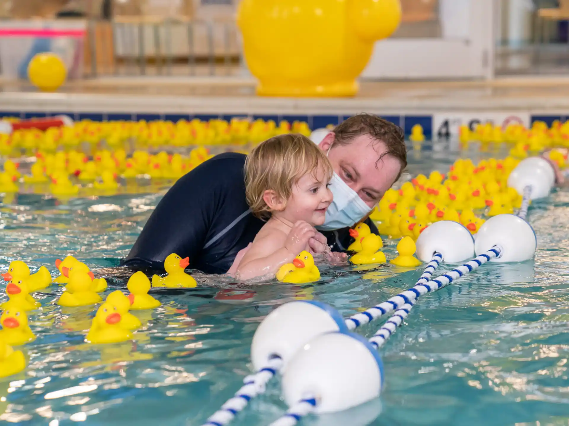 a person and a child in a pool with rubber ducks