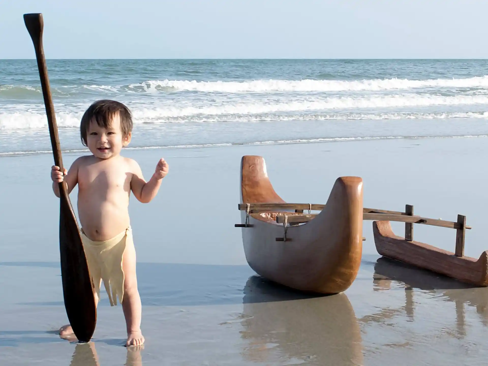 a boy holding a stick and standing in water next to a boat