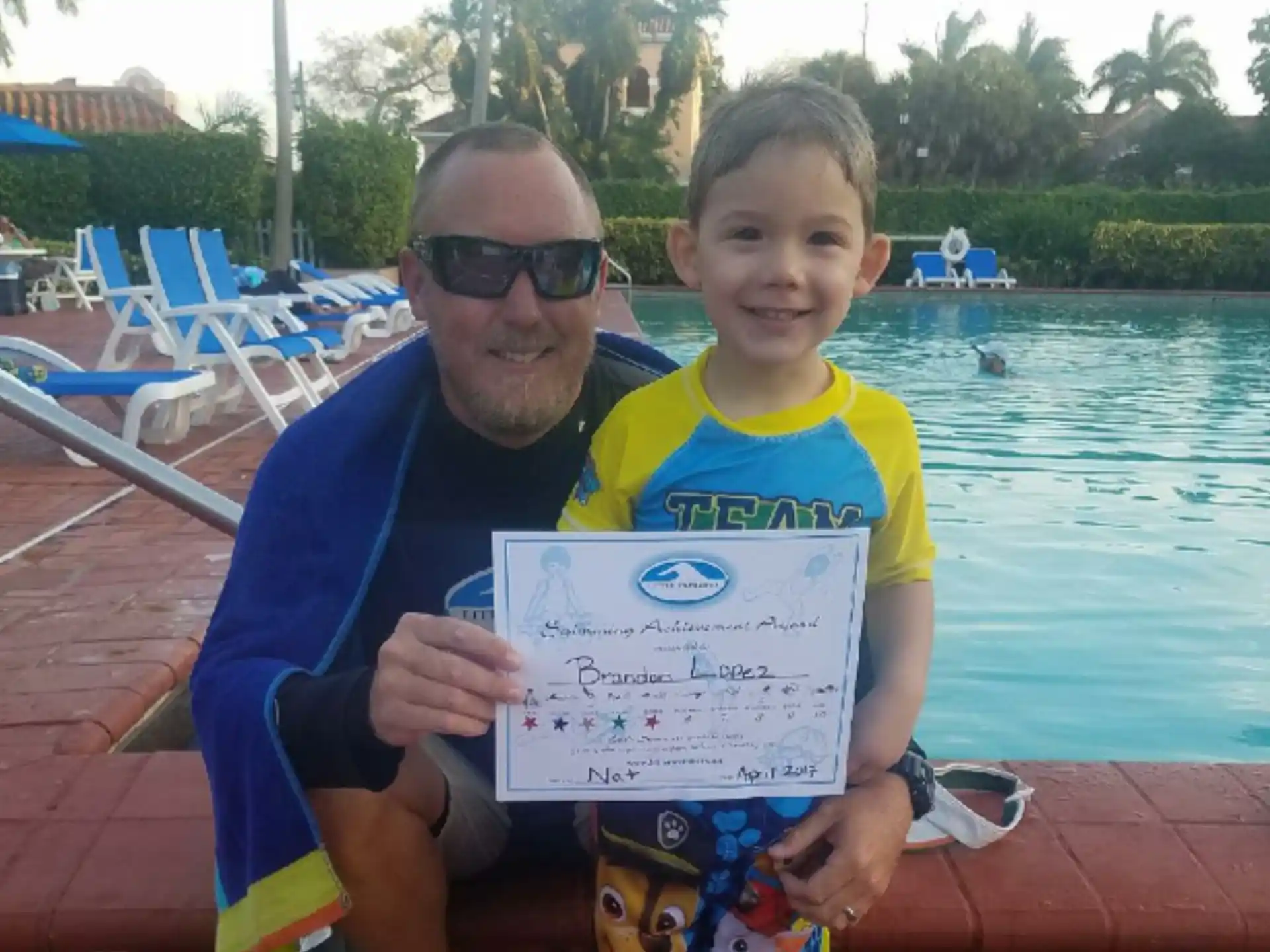 a man and a boy holding a sign by a pool
