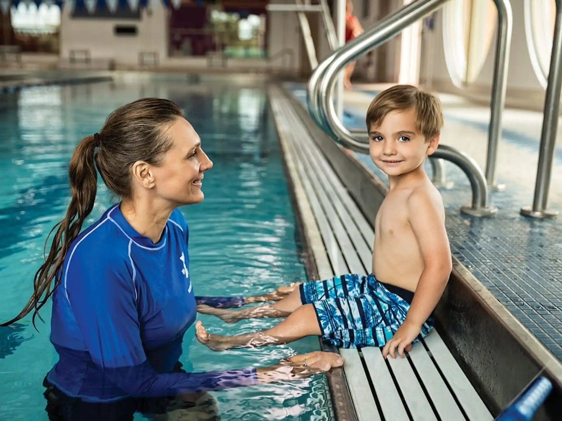 a person and a boy sitting on a dock by a pool