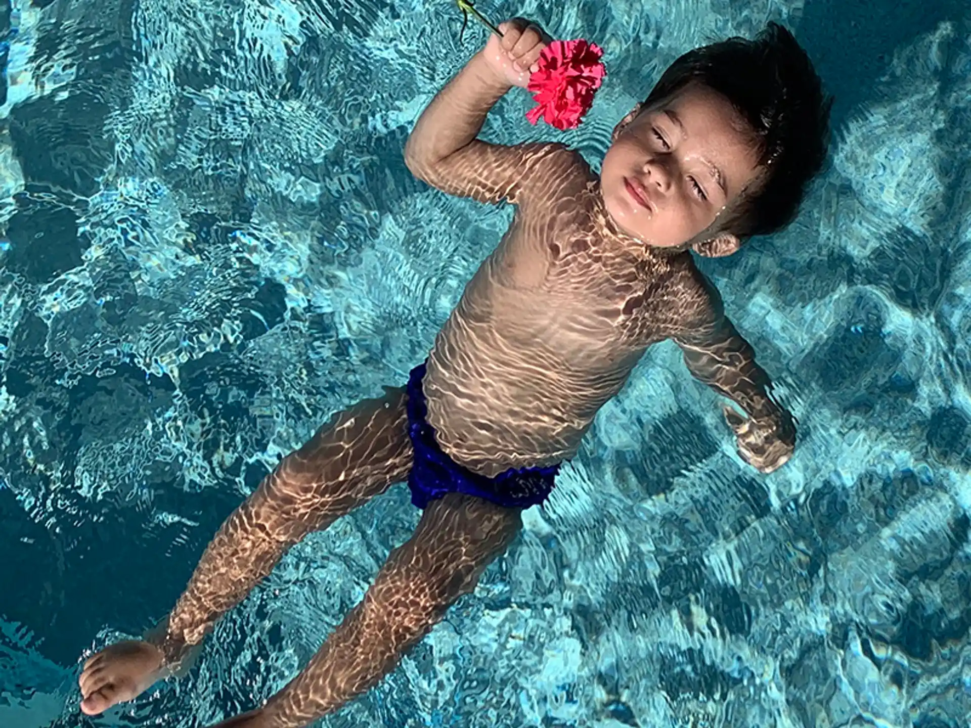 a boy in a swimsuit holding a rose in the water