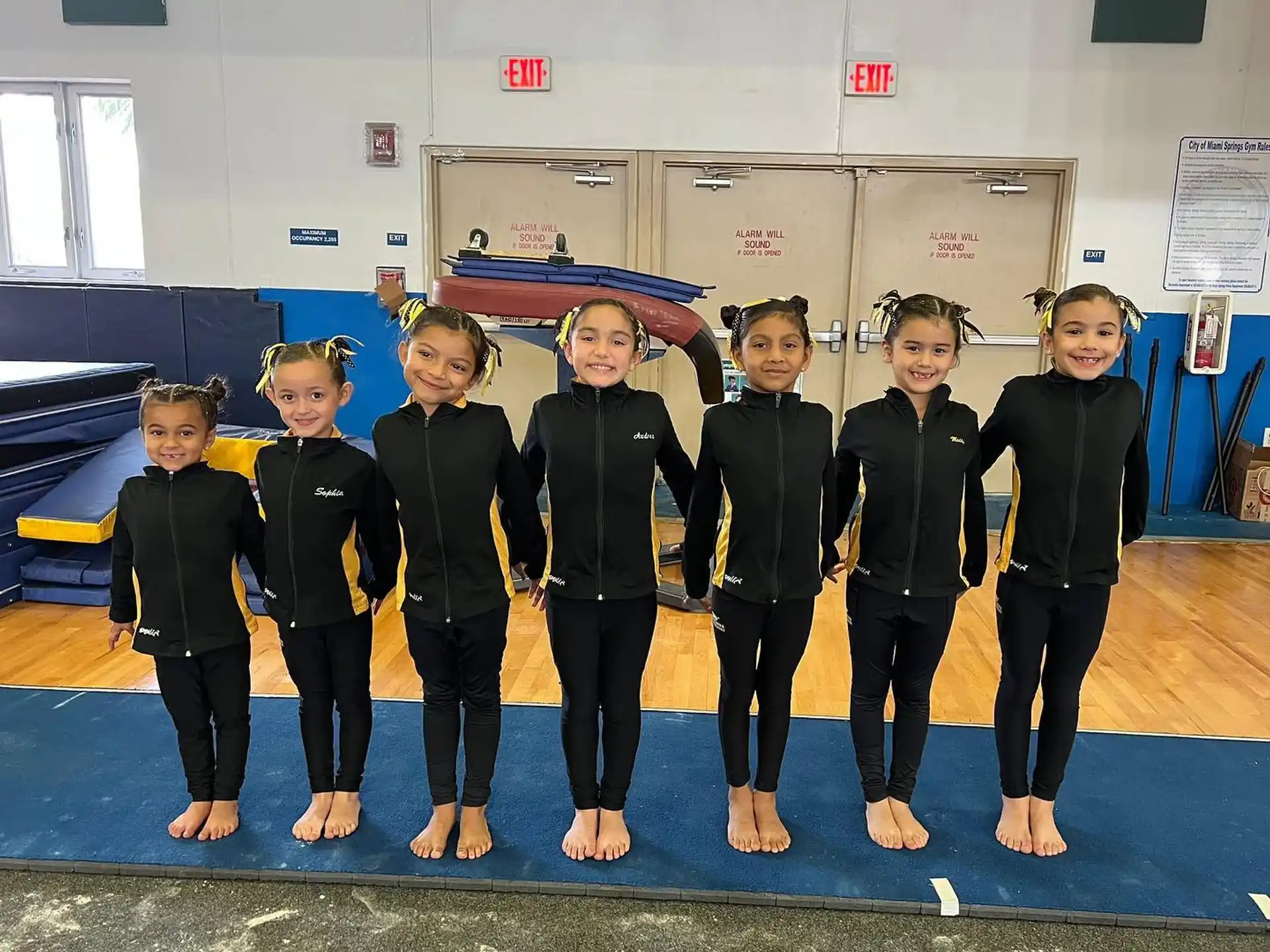 a group of children in black and yellow uniforms standing on a mat