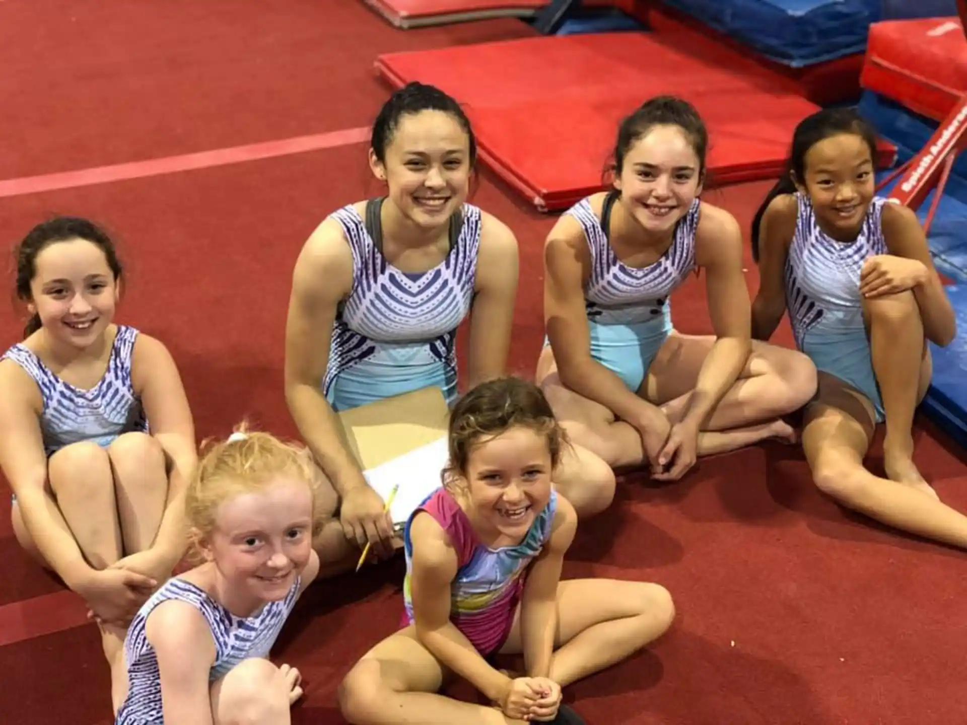 a group of girls in swimsuits sitting on a red mat