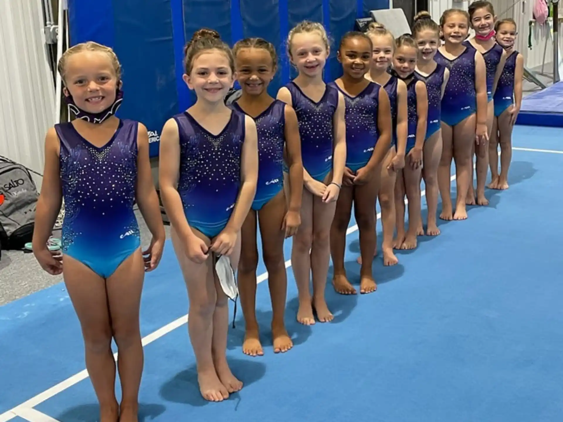 a group of girls in leotards standing on a blue mat